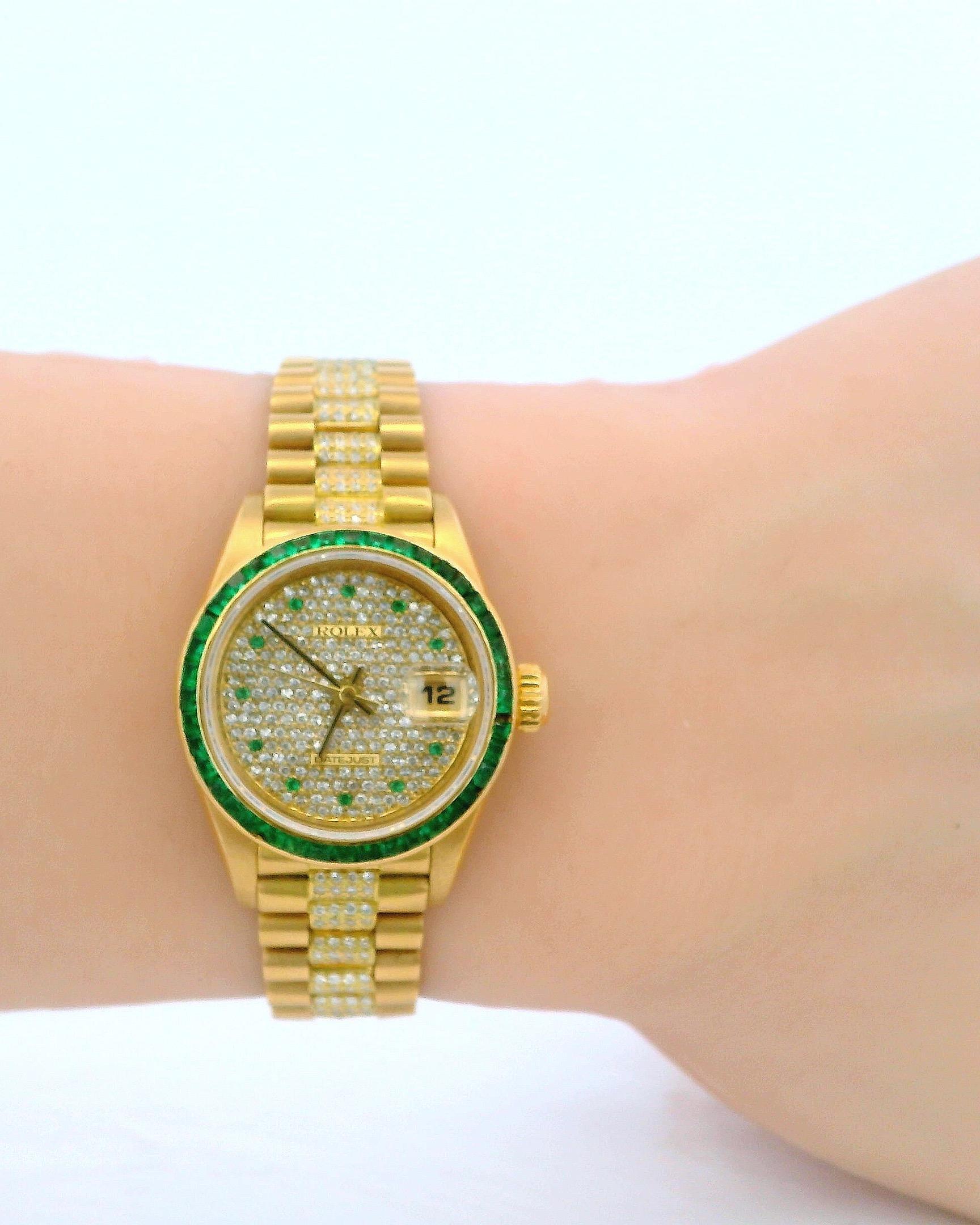 Rolex präsentiert eine feine und seltene Damenarmbanduhr aus 18-karätigem Gold mit exquisiten Diamant- und Smaragdfassungen. Diese Uhr verfügt über ein Automatikwerk mit Sekundenzeiger in der Mitte und Datumsfunktion, begleitet von einem Armband mit