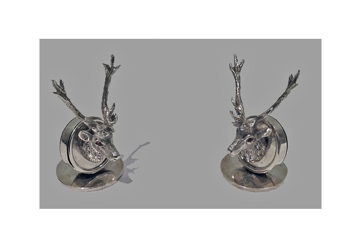 Pair of Asprey English silver stag menu place card holders, London 1925. The holders are of disc shape, each surmounted with a stag's head inset with cabochon red eyes. Fully hallmarked and stamped Asprey. Height: 2 1/4 inches. Weight: 104 grams.