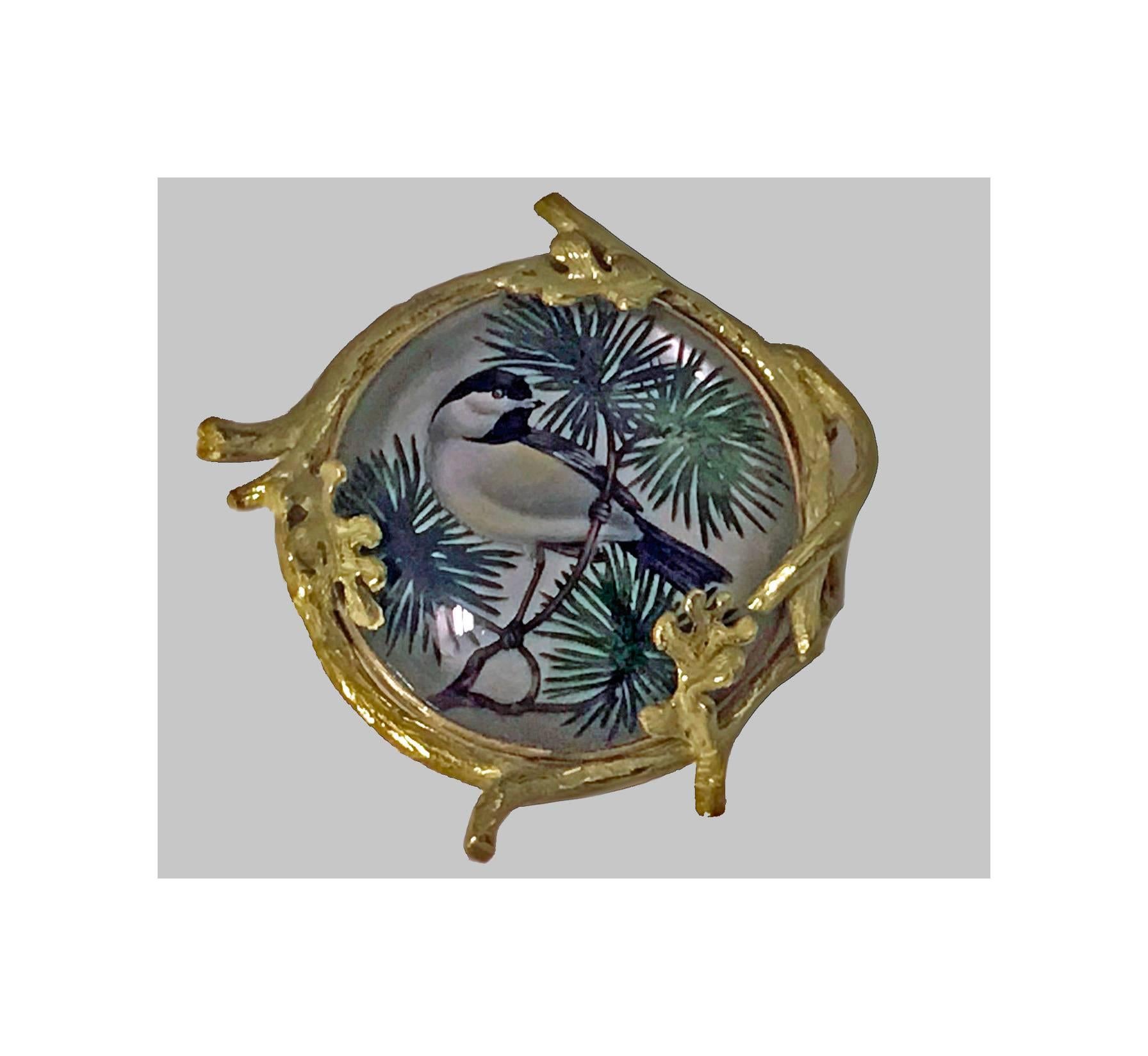 Very fine 18K Reverse Intaglio Painted Crystal Pendant Brooch depicting a finch on a pine bough, realistically textured gold mount with twig and leaf motifs. Hinged bale pendant and safety catch to pin at reverse. Measures: 1.375 x 1.50 inches.