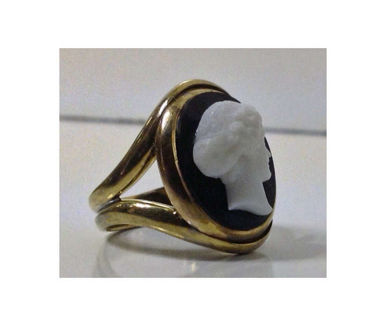 Antique Stone Cameo Ring mounted in 18K, England C.1875. The ring, bezel set with black and white stone cameo depicting the profile of a young woman, plain splay shank, stamped 18K. Total Item Weight:- 9.36 gms.  Cameo and setting C.1875, shank