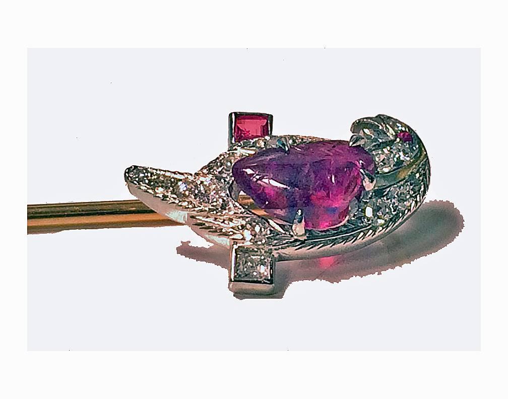 Tiffany Platinum Ruby and Diamond Parrot on gold stickpin, C.1940. The stickpin depicting a parrot sitting on a ruby and diamond set perch, the carved ruby body realistically textured, the crown, beak and tail encrusted with small diamonds and small