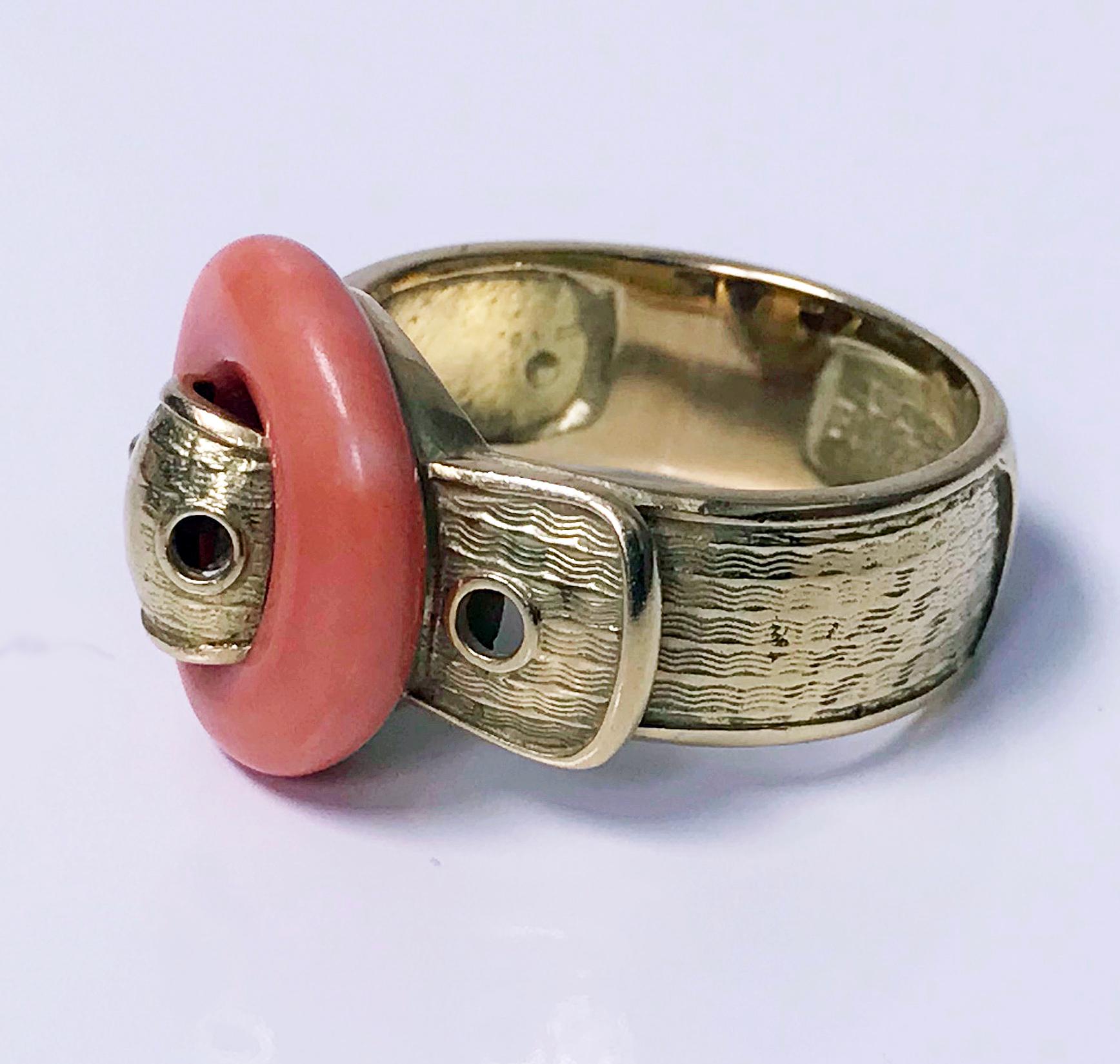 1970’s Piaget 18K Ring. The Ring of 18K yellow gold textured buckle form, the top of `buckle’ with round salmon pink color. Signed Piaget 750 and English import mark for 1974. Total Item Weight: 12 grams. Ring Size: 9. (May be sized). 