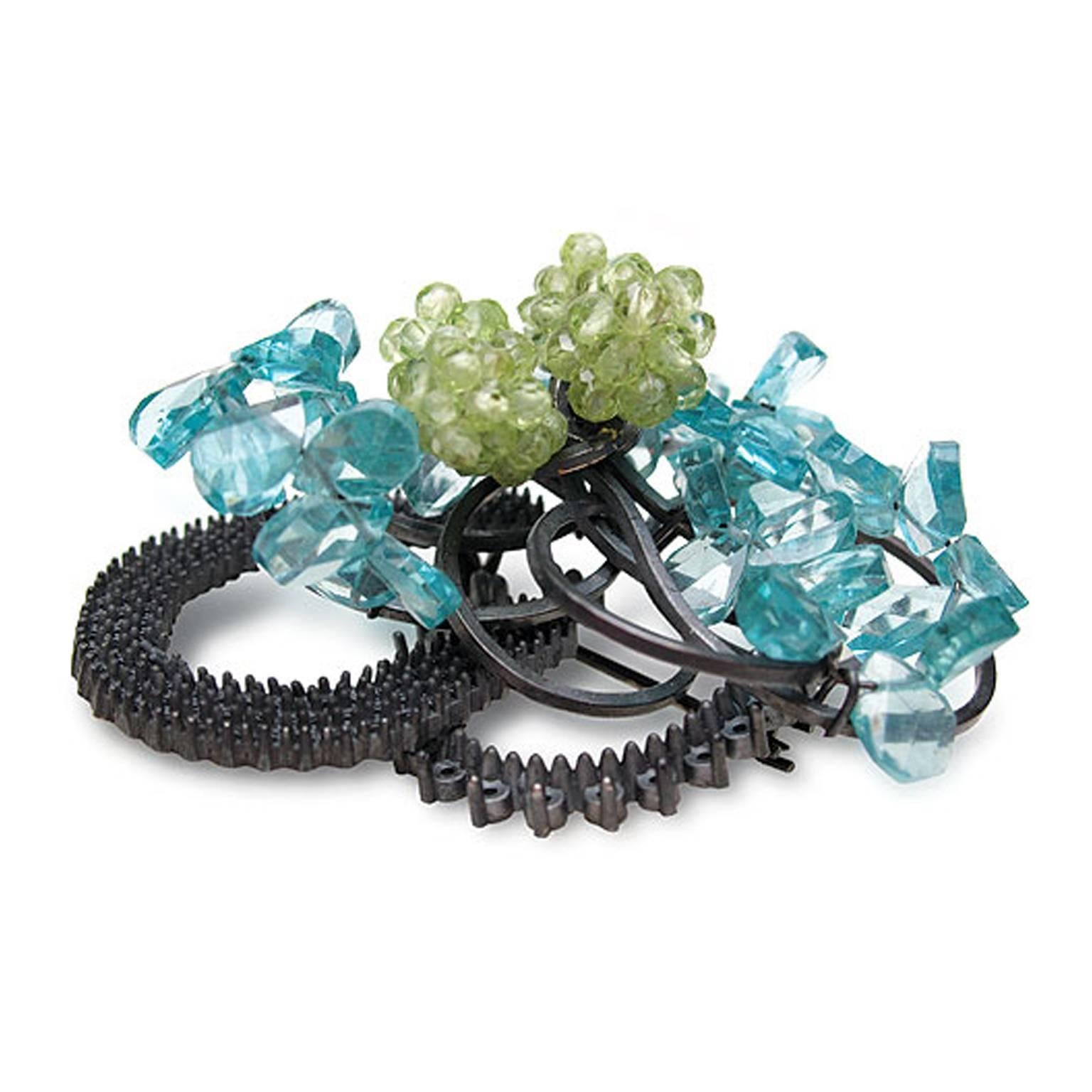 Sculptural clusters of Peridot and Apatite are set against a backdrop of entwined blackened sterling silver. This beguiling brooch is hand-crafted in her London studio by Donna Brennan.

Donna's work typically features jewellery & sculpturally