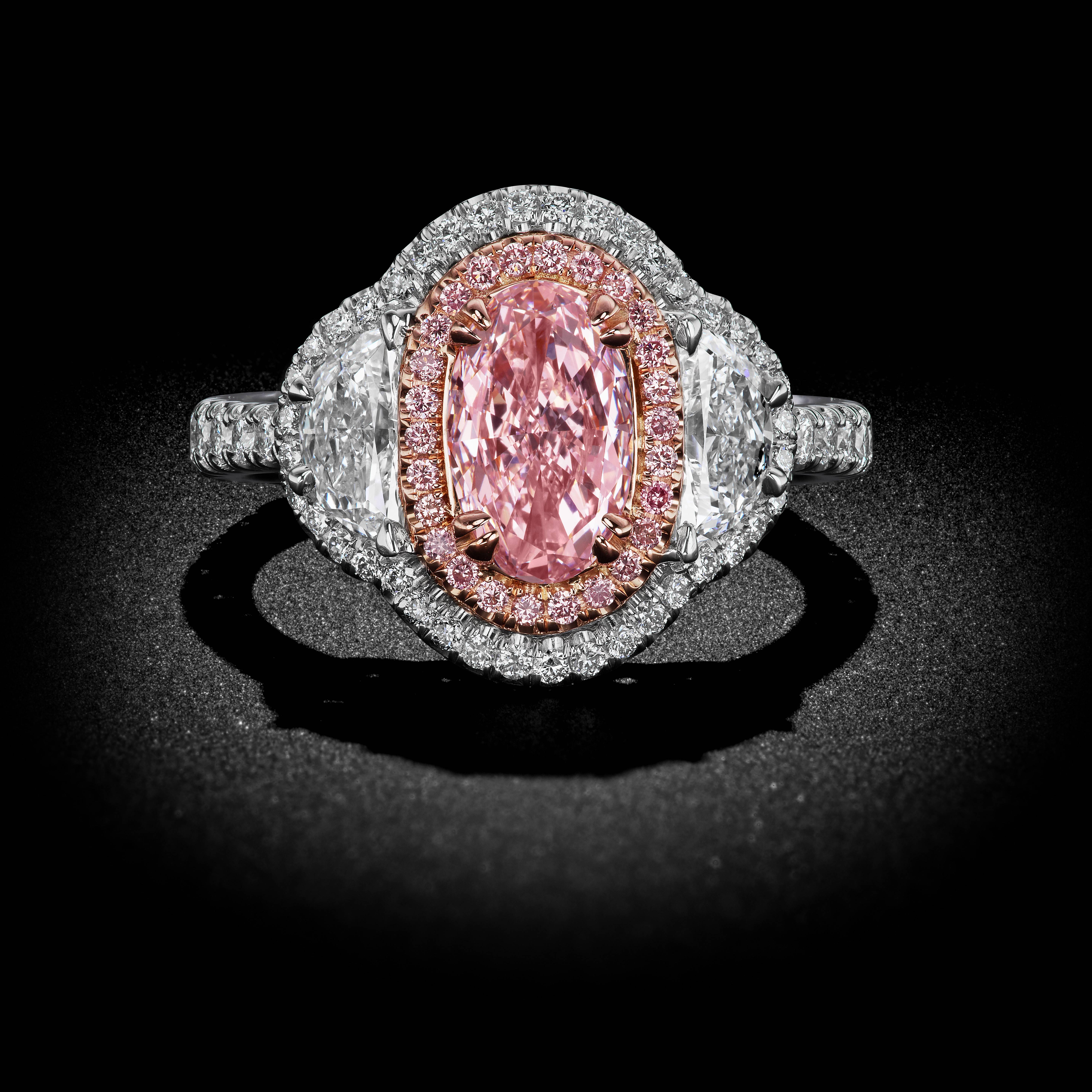 A delicate setting of bright Platinum and 18k rose gold gleams alight with brilliant white Diamond Pavé accents. A rare GIA certified Pink 1.00 ct Oval cut Diamond rests at the center accompanied by two half-moon white Diamond side-stones totaling