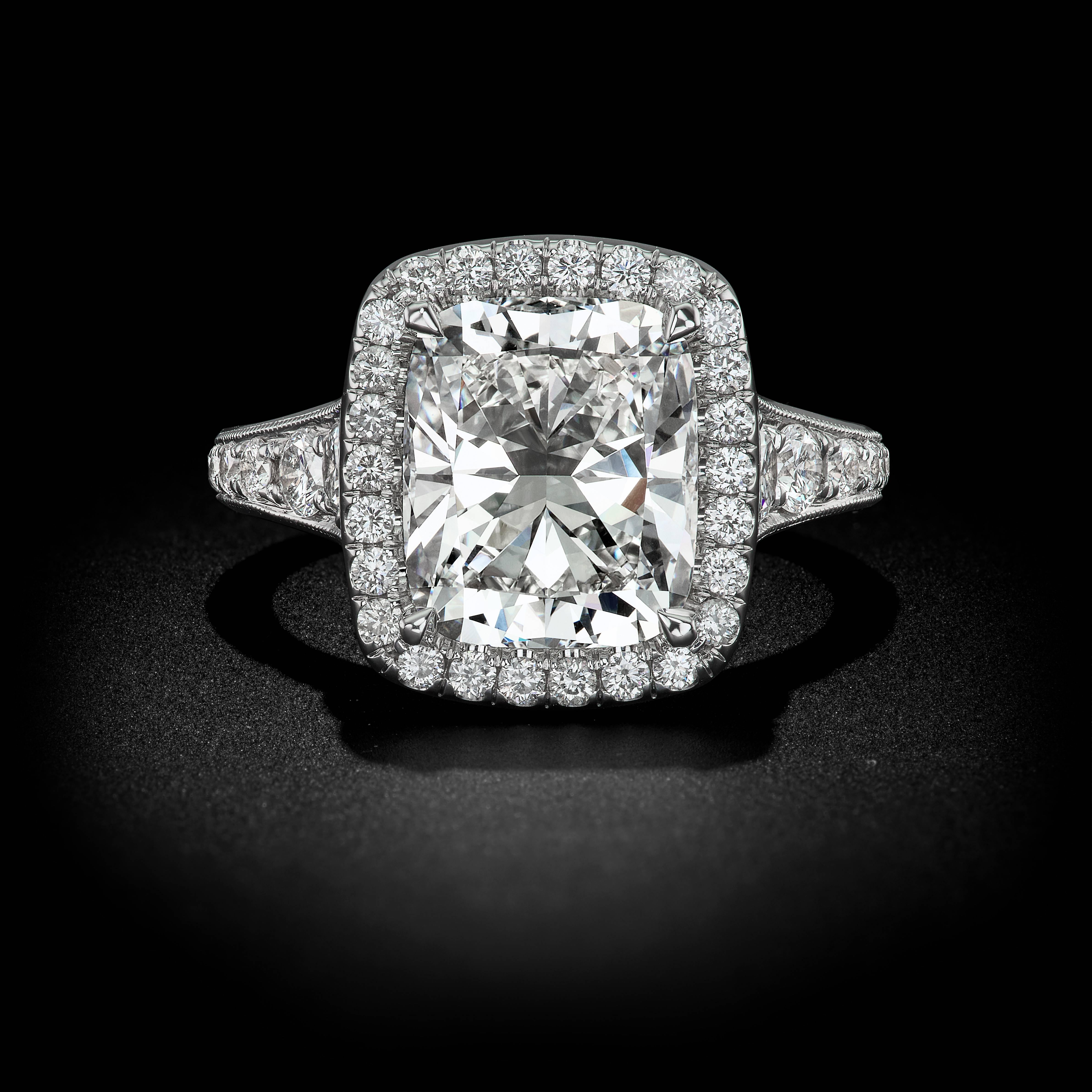 This intriguing design combines multiple settings to capture the heart. A band of 18k white gold embraces graduating channel set Round Brilliant accents and a Pavé Halo as a beaming 4.12 Carat Cushion Diamond emanates a superior display of light