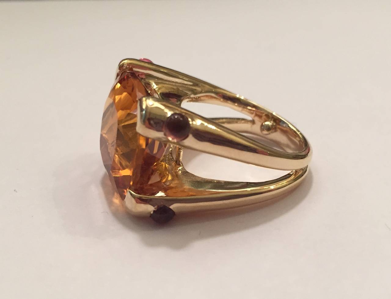 18kt Yellow Gold Cushion Ring with 15mm Orange Citrine (approximately 25 cts) and four Cabochon Pink Topaz (approximately 0.40 cts)..
Center faceted Citrine has an orange tone offset by the soft pink cabochon pink topaz accent stone.  The elegant