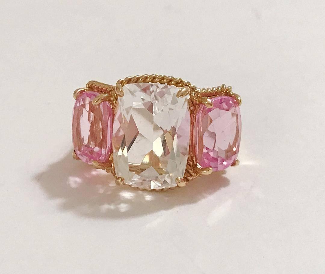 Elegant 18kt Yellow Three Stone Ring with Rope Twist Border with split shank detail. The ring features a center faceted cushion cut Rock Crystal and two cushion cut Pink Topaz stones surrounded by twisted gold rope. The center Rock Crystal stone