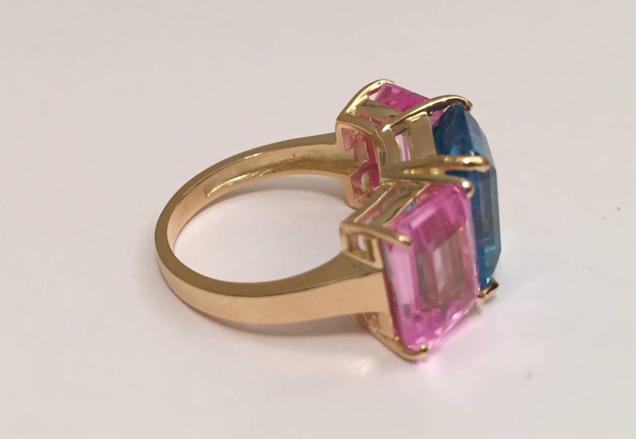 Elegant 18kt Emerald cut Three stone ring with bright Blue Topaz and Bright Pink Topaz.  A fabulous Cocktail ring!  

The emerald cut RIng measures approximately 1 1/4 inch across the top of the ring.

This ring can be sized to an ring size.

The