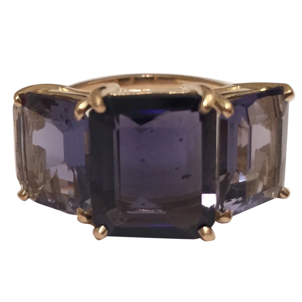 Questo audace anello a tre pietre in oro giallo 18kt con taglio smeraldo e tre ioliti è un fantastico anello per tutti i giorni.  La Iolite centrale ha una tonalità leggermente più profonda rispetto alle due Iolite esterne che creano