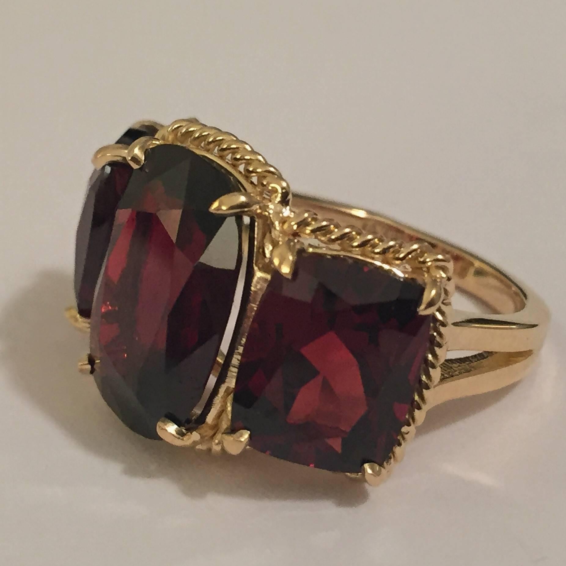 Elegant 18kt Yellow Three Stone Ring with Rope Twist Border with split shank detail. The ring features three faceted cushion cut Garnet stones surrounded by twisted gold rope. The center Garnet stone measures 5/8