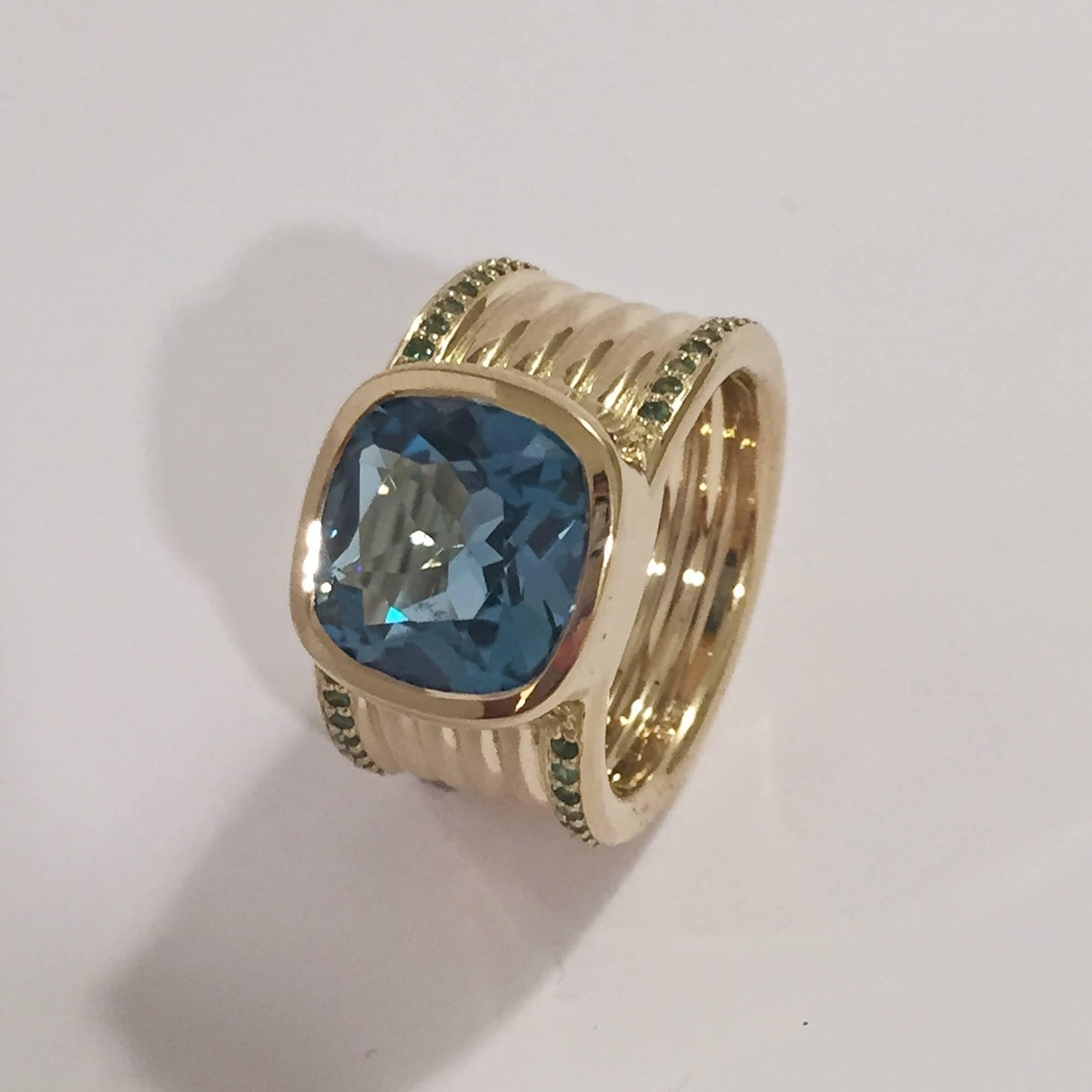 18kt Yellow Gold Cigar band ring with center faceted deep Blue Topaz and Tsavorite Green Garnet accents on the outer rims.

The Wide band ring is fluted with four ribbed bands down the middle of the ring.
The band is 1/2" wide.

The ring