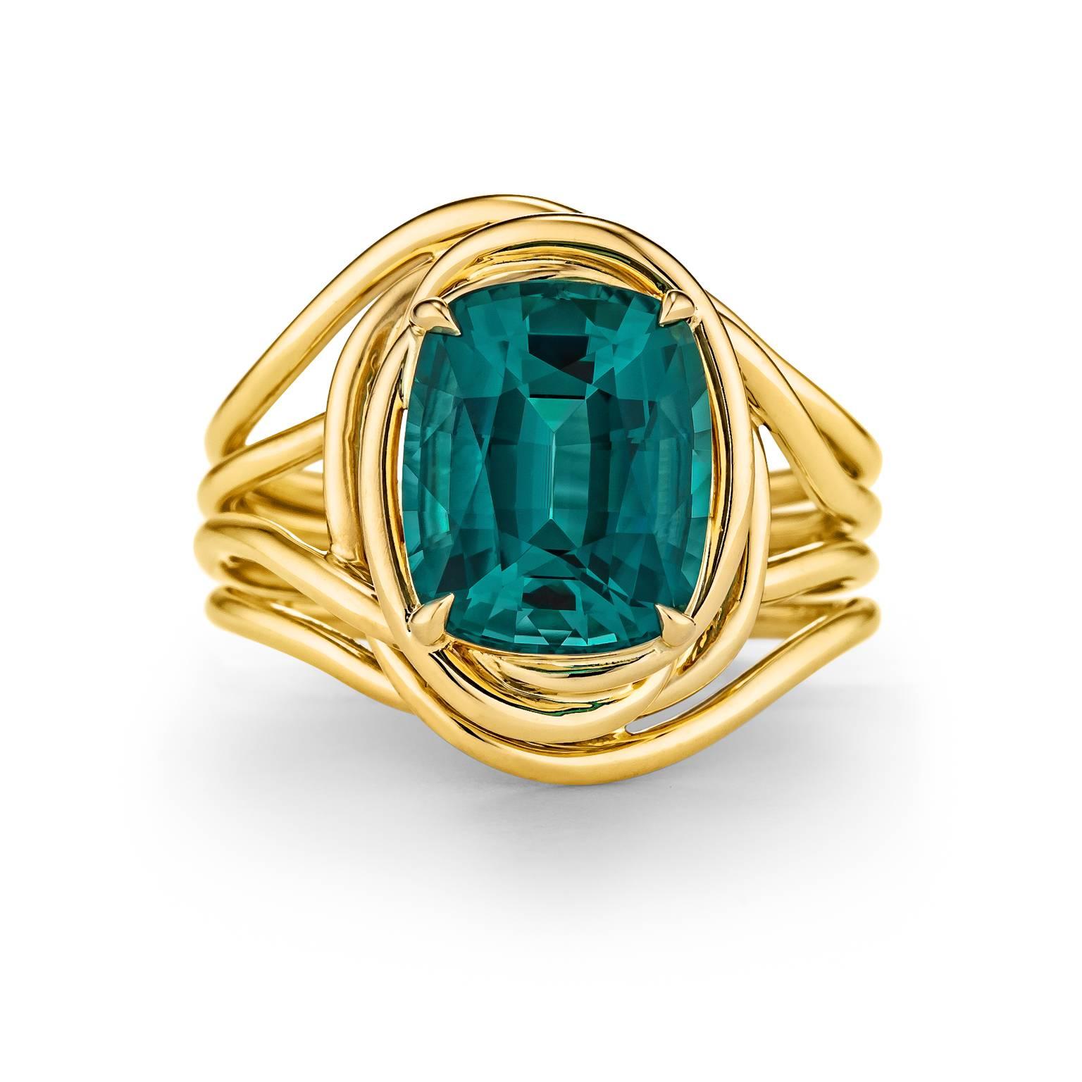 This 3.68 carat cushion cut indicolite tourmaline is the velvety blue/green color of a royal peacock.  Mounted atop four 18 karat yellow gold organically intertwined gold ropes, this precious gemstone's color is dreamy to look at and magical to