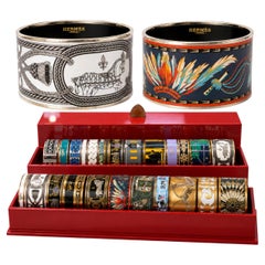26 bracciali rigidi vintage Hermès con motivi smaltati, in diverse larghezze e con i relativi espositori