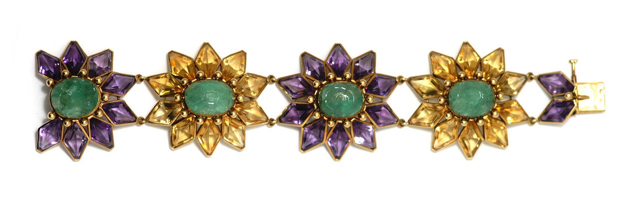 An unusual and chunky 18kt yellow gold link bracelet, presenting interconnected  large flower motifs elements in citrines and amethysts, highlighted by central carved emeralds. Circa 1980