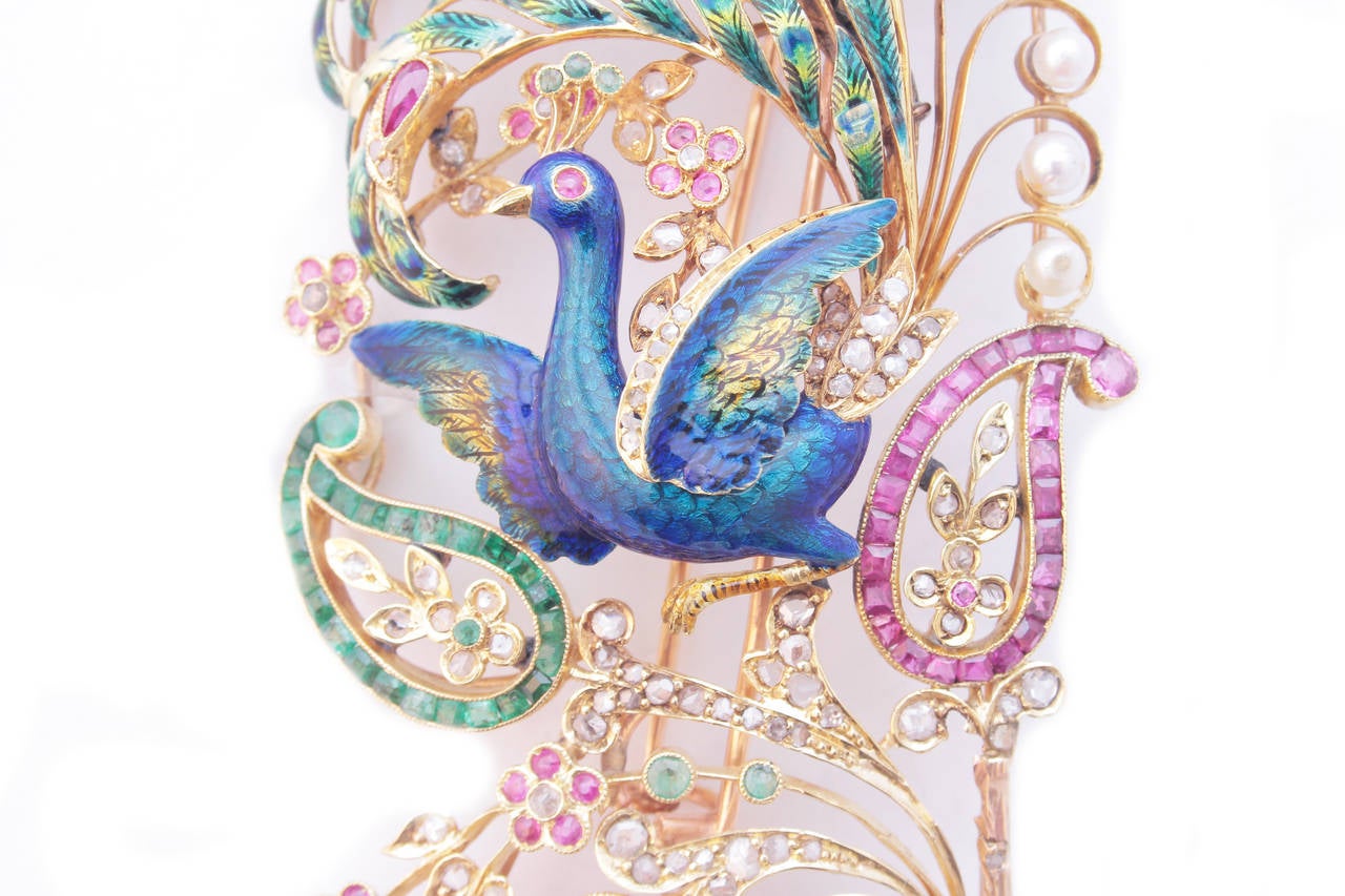 A tall and exquisitely crafted Art Nouveau Brooch representing a fantasy bird immersed in floral decorations, embellished by fine enamelling, pearls, rubies, emeralds, and diamonds on an 18kt yellow gold mounting. France, circa 1900.