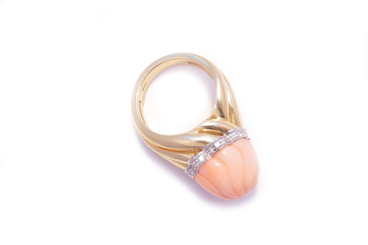 A vortex shaped 18kt yellow gold ring sustaining a pink coral top carved in accordance, embellished by a diamond on white gold band. Adjustable size. Italy, circa 1960.