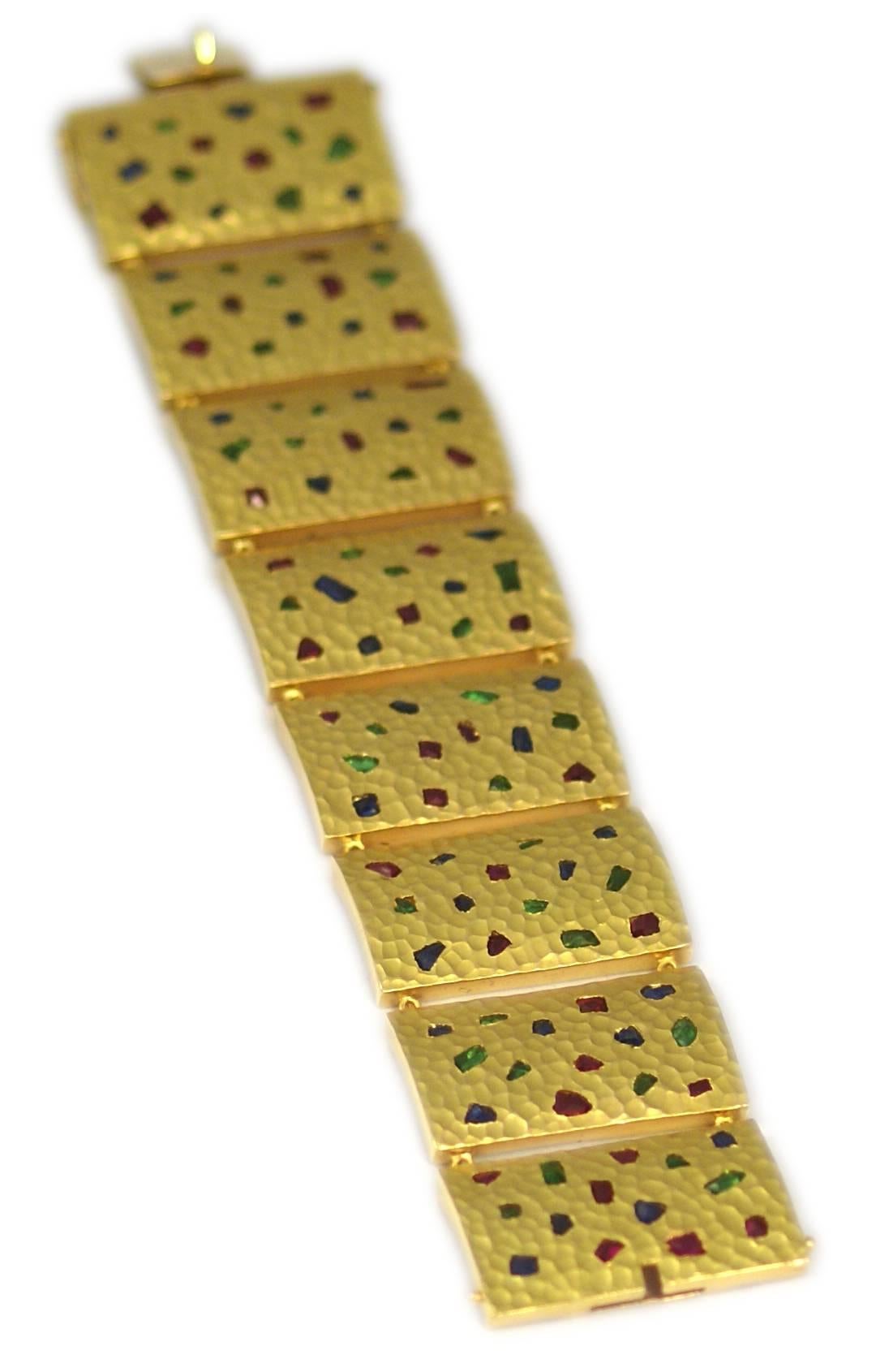 A peculiar 18kt hammered yellow gold bracelet composed of rectangular interlinked elements, embellished with irregular cut emeralds, rubies and sapphires. Circa 1970
