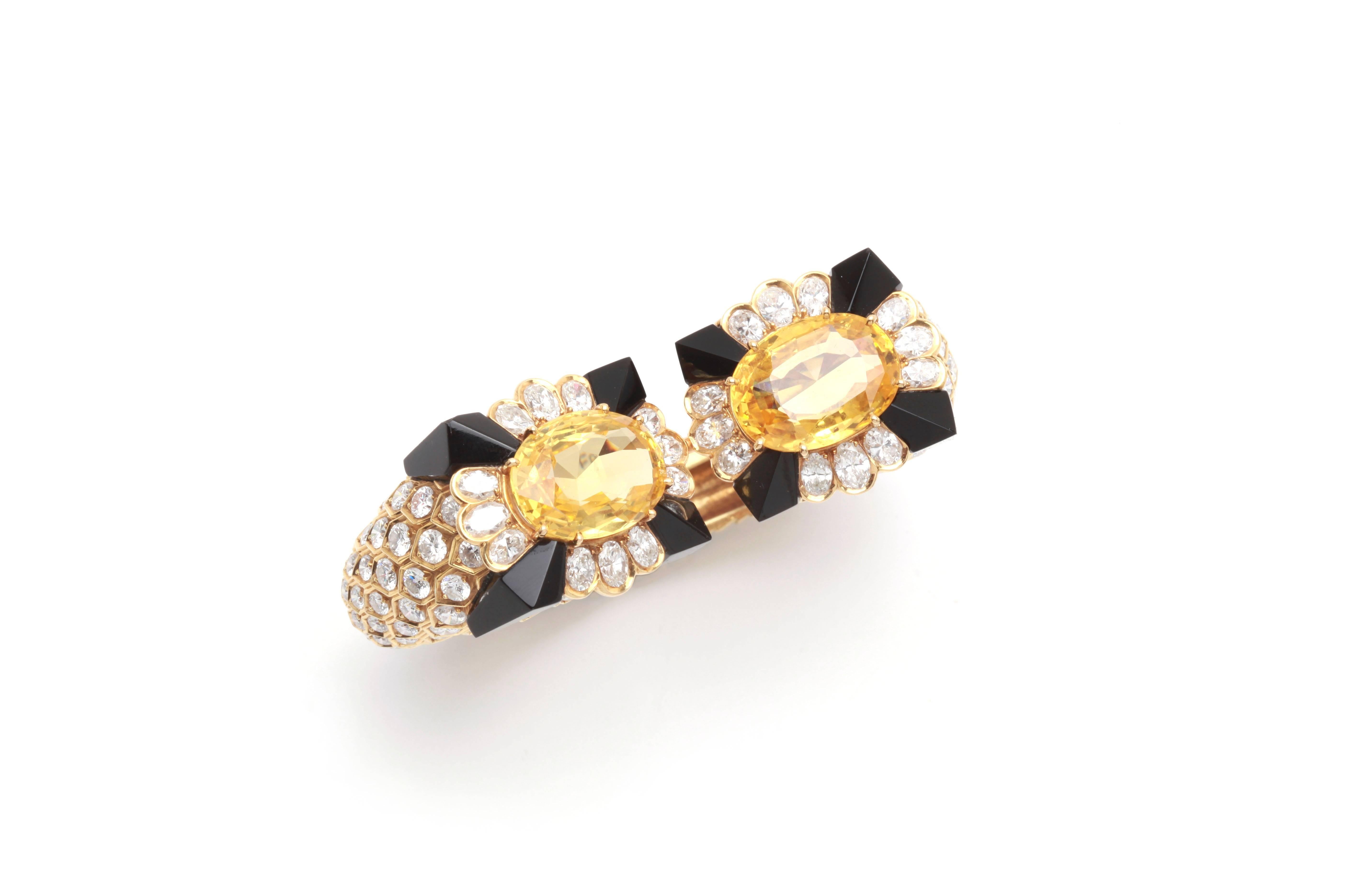 A superb bracelet by esteemed French jeweler Fred, showcasing two large cushion shaped yellow sapphires, mounted on a scaled 18kt yellow gold cuff, highlighted with diamonds and onyx elements. Circa 1970.
