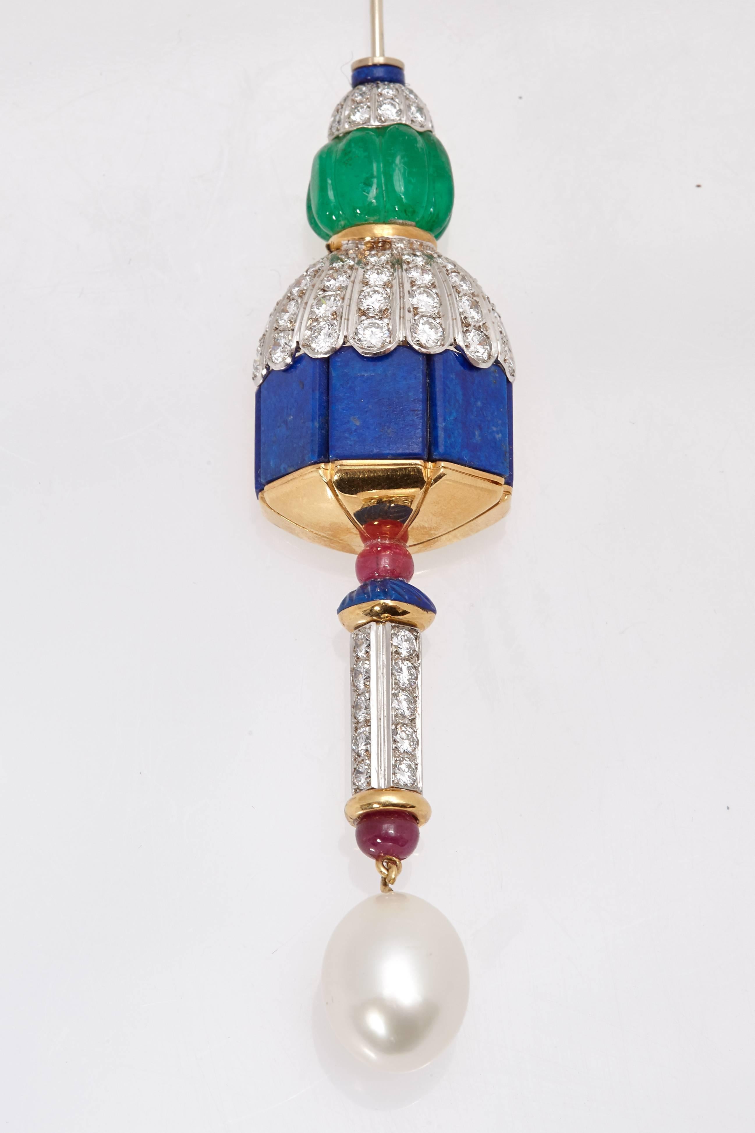 An unusual and bejeweled jabot pin with carved emeralds, diamonds, lapis, rubies and dangling pearl, mounted on 18kt yellow gold and platinum. Made in Italy, circa 1970.