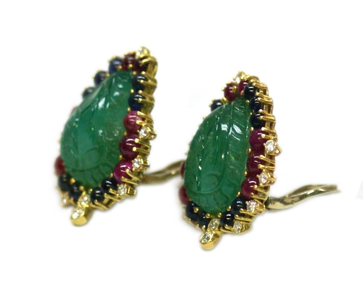 A pair of ear clips of foliate design, the main body consisting of two carved emerald leaves, highlighted by cabochon rubies, cabochon sapphires and diamonds, on an 18kt yellow gold mounting. Circa 1965