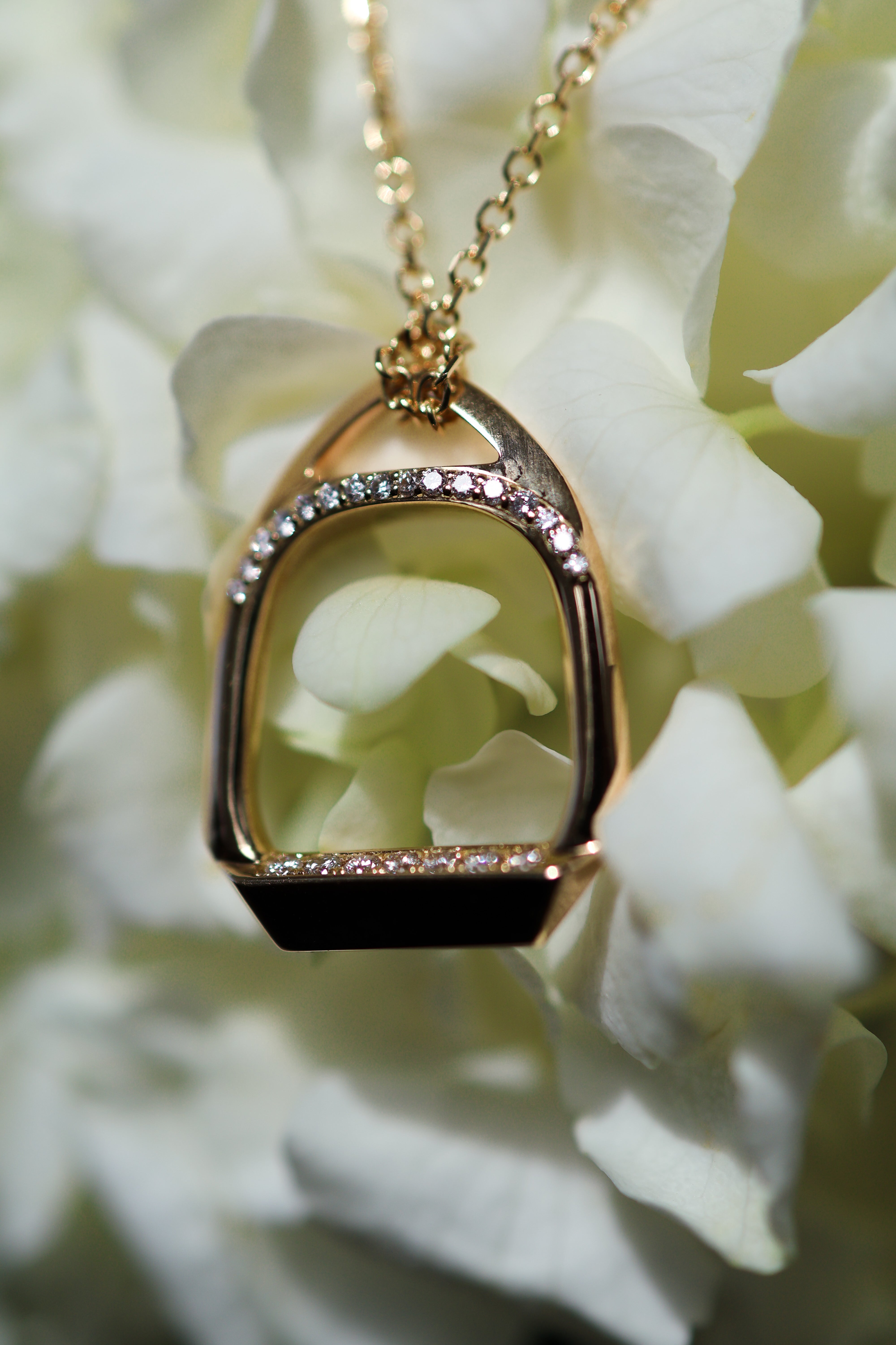 This exquisite stirrup necklace showcases a captivating bridge of front-facing diamonds, flawlessly accentuated by a row of diamonds along the foot pad. The 18k yellow gold chain adds a touch of warmth and sophistication to this enchanting piece.