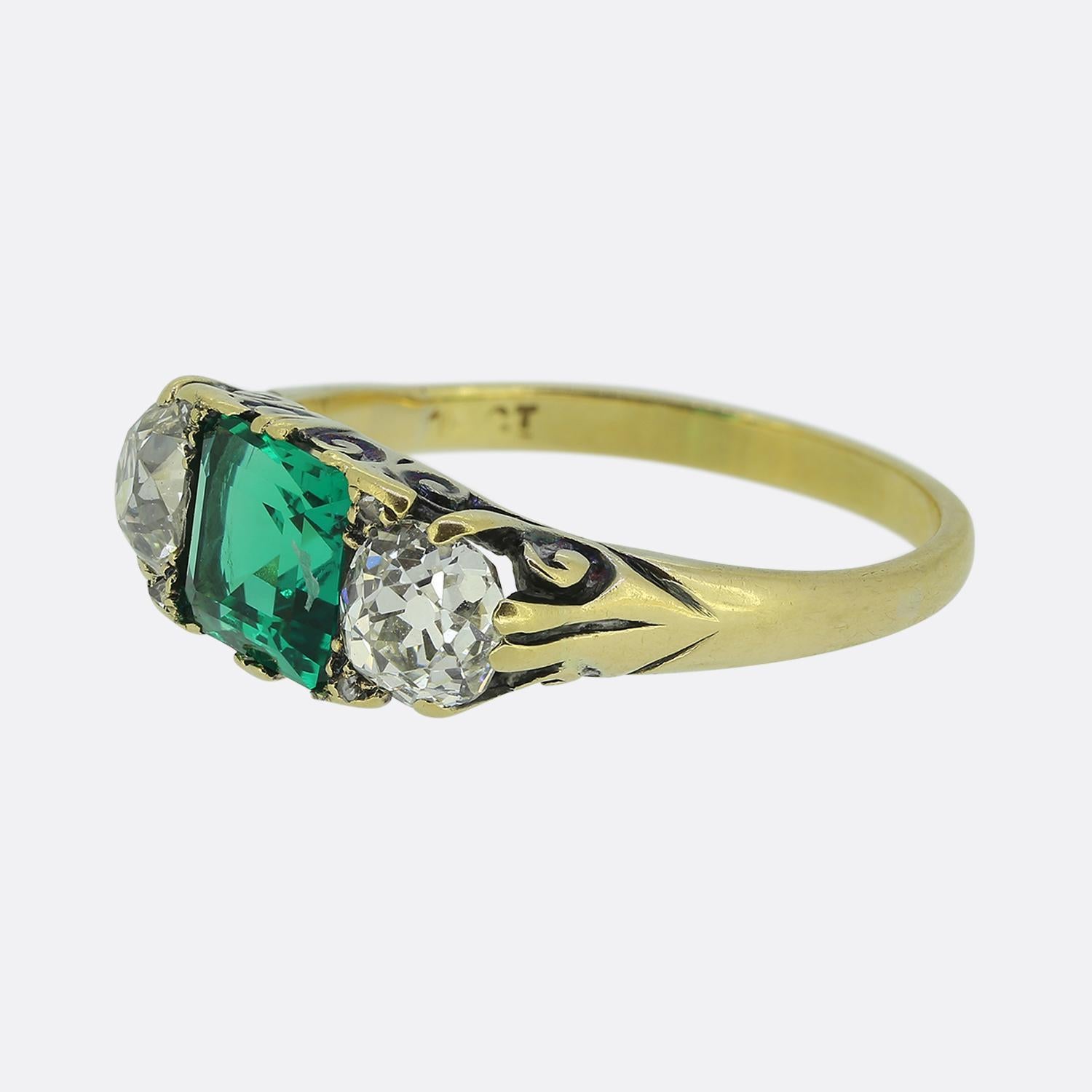 Hier haben wir einen wunderschönen viktorianischen Ring mit drei Steinen. Dieses antike Stück zeigt einen leuchtend grünen Smaragd im Achteckschliff in der Mitte der Vorderseite. Dieser auffällige Hauptstein wird auf beiden Seiten von einem