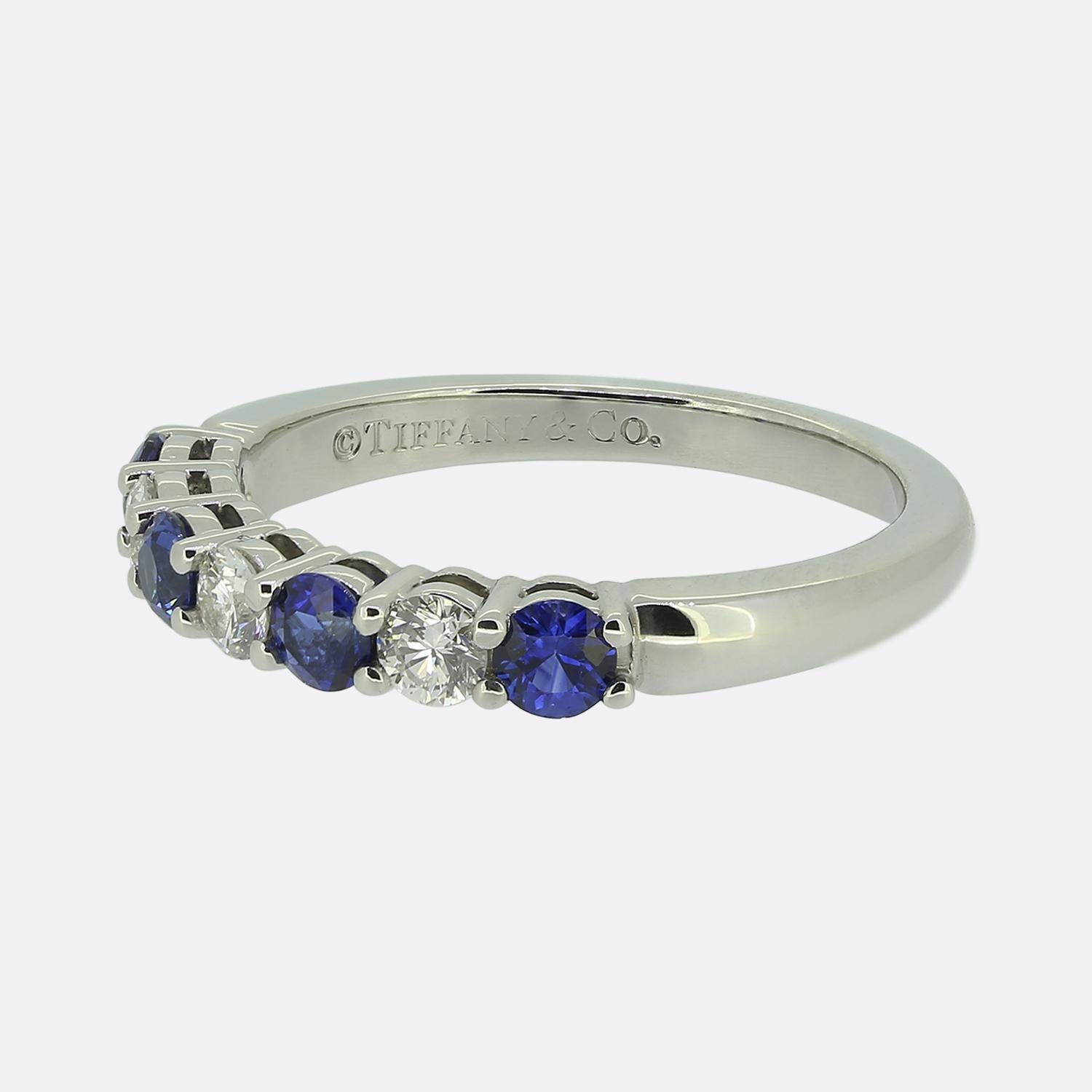 Ecco un raffinato anello con sette pietre di Tiffany & Co., gioielliere di fama mondiale. Il design presenta un'alternanza di zaffiri blu rotondi sfaccettati e diamanti bianchi taglio brillante, creando un contrasto sorprendente. Ciascuna pietra è