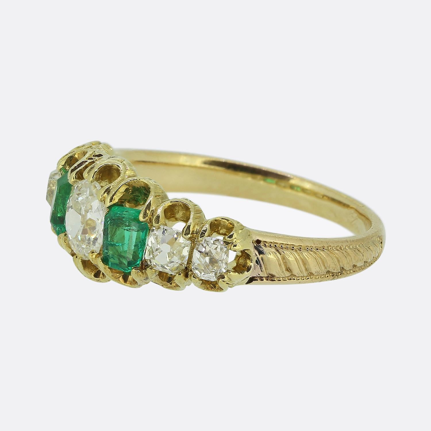 Nous avons ici une bague victorienne à sept pierres de style classique. Cette pièce ancienne présente un mélange harmonieux d'émeraudes et de diamants, avec deux émeraudes d'un vert vibrant flanquant un diamant ovale à facettes d'un blanc éclatant,