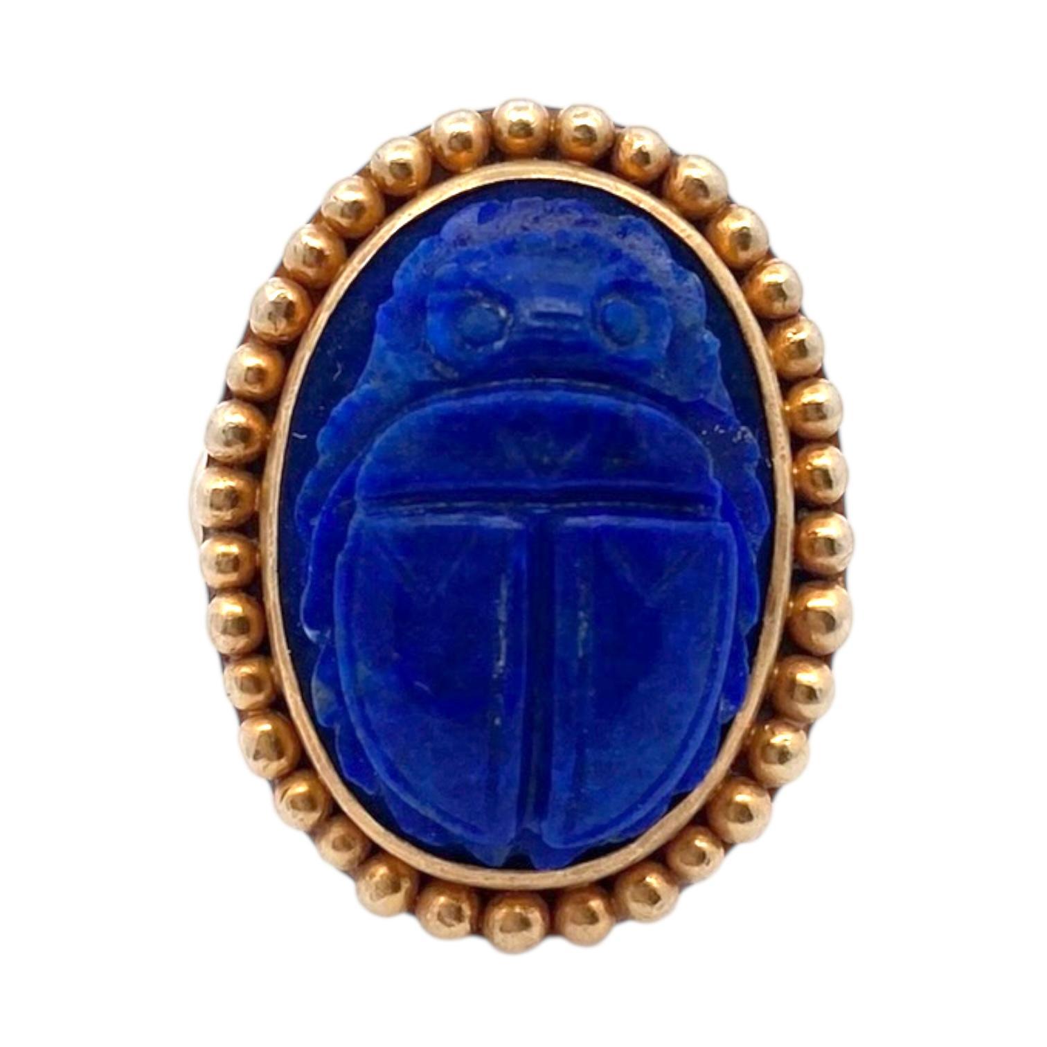 Realizzato in oro giallo 18 carati, questo audace anello presenta un sorprendente motivo a scarabeo con lapislazzuli tagliati a cabochon. La pietra blu intenso è intagliata in modo intricato in stile revival egiziano e incastonata in una cornice