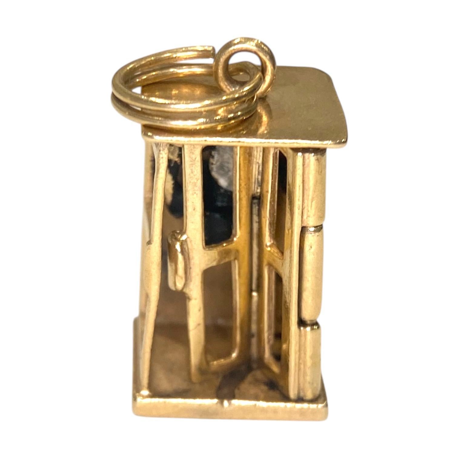 Breloque vintage en or jaune 14 carats, représentant une cabine téléphonique miniature avec des détails complexes. Le charme comprend un téléphone émaillé sur le mur du fond et une porte articulée. La breloque est compacte et bien fabriquée, adaptée