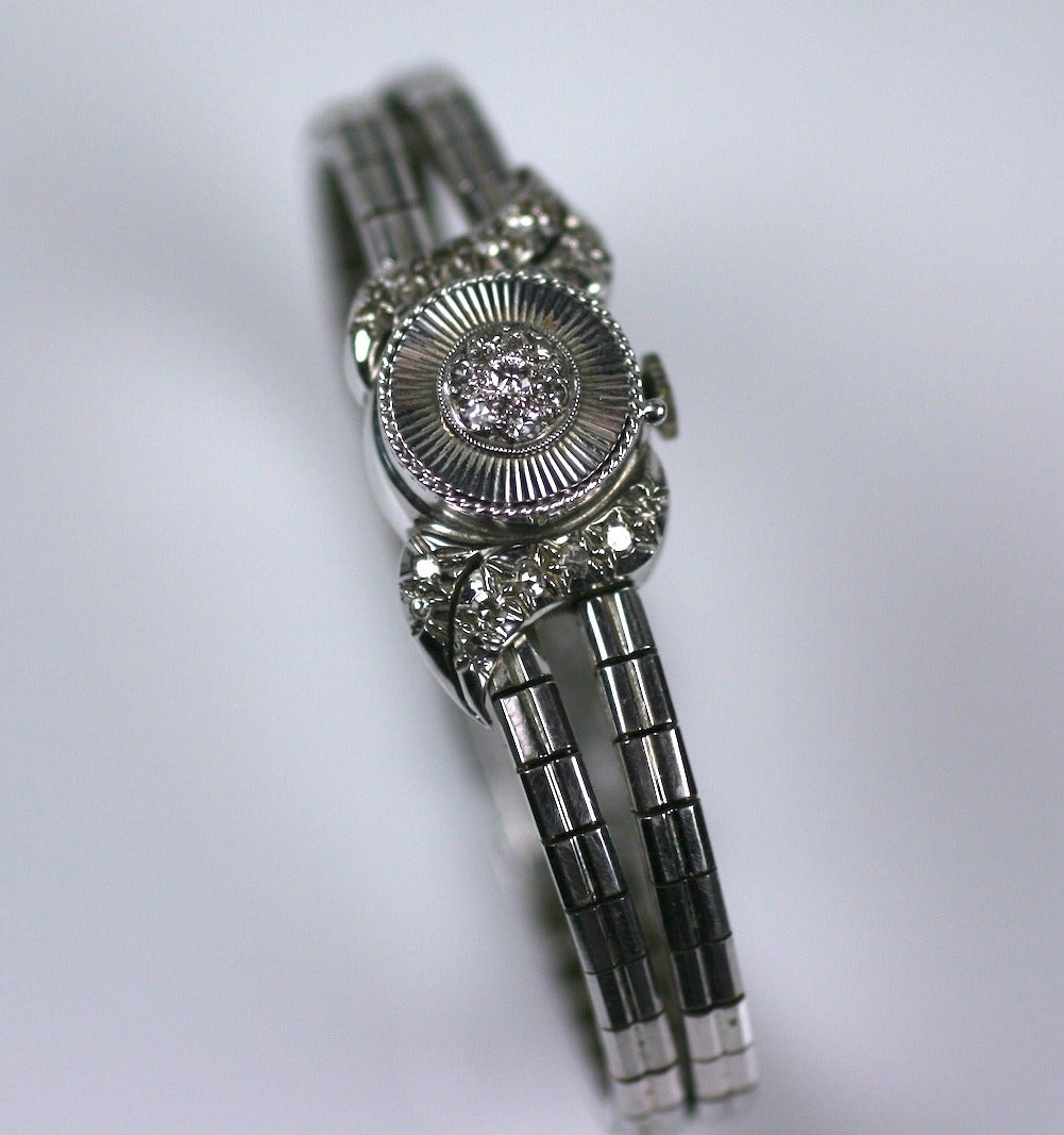 Elegant Retro cocktail bracelet in white gold and diamonds with covered watch. Cover has a center cluster of diamonds in a ribbed circle with pave diamond leaves on each side. 
Articulated double link forms bracelet. Movement signed 