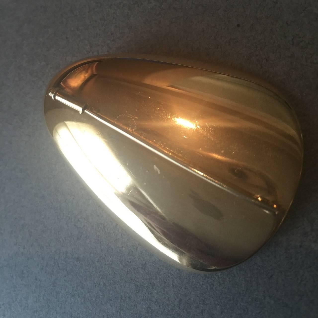 Georg Jensen Brooch/Pendant by Nanna Ditzel, no. 1328.

Shell design in 18kt gold with pearl. Sliding tubular clasp with hole to convert to a pendant. 

Images show pendant on a Georg Jensen braided leather rope with sterling silver clasp which