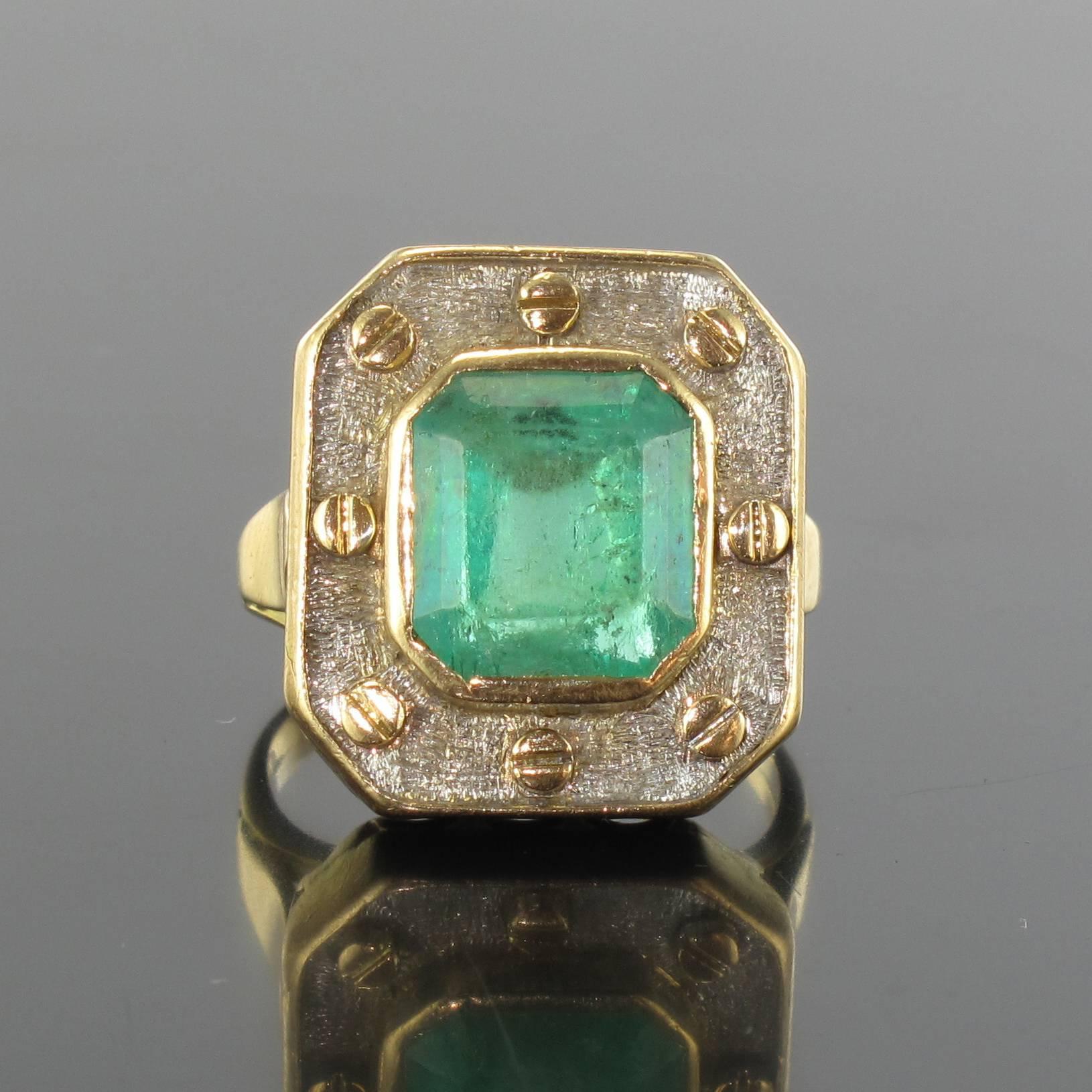 Ring in 18 carat white and yellow gold, eagle head hallmark. 

An imposing emerald ring formed of a chiselled white gold bed holding a bezel set emerald accentuated by the surrounding 8 yellow gold screw heads. The openwork bed allows light to