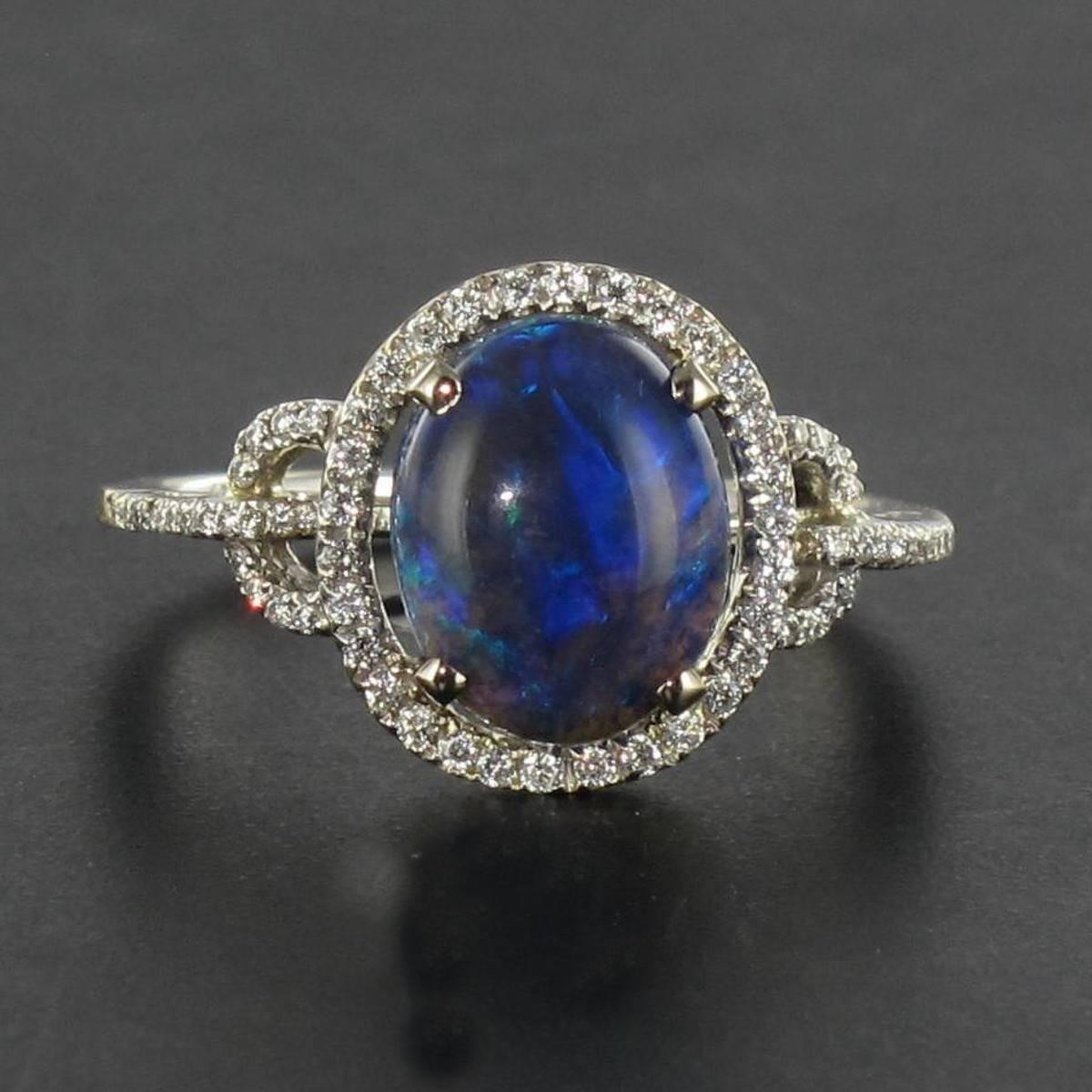 Ring in 18 carat white gold. 

This gorgeous opal ring features a claw set oval shaped black opal cabochon from Australia with a halo of small brilliant cut diamonds. The shoulders of the white gold ring band are formed of semi-circles again set