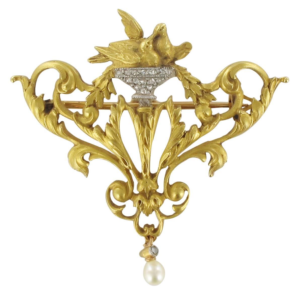 Brooch in 18 carat yellow gold, eagle head hallmark. 

Featuring an openwork leafy design topped with a pair of doves in a nest set with rose cut diamonds. Suspended from this motif is a pearl with a rose cut diamond cap. Two small rings at the