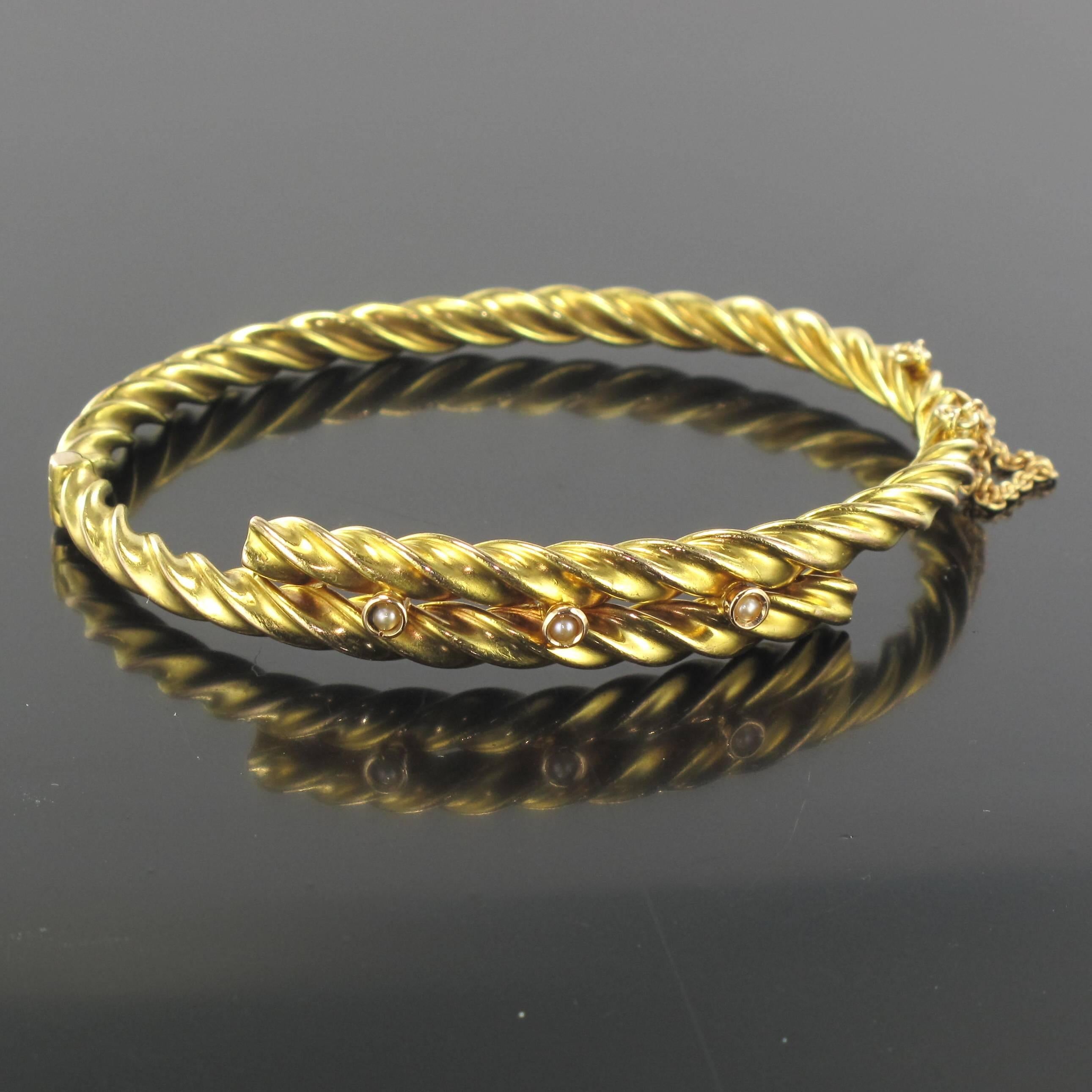 Bracelet in 14 carat yellow gold.
A striking antique oval bracelet composed of twisted gold that overlaps at the top. This bangle bracelet is set with 3 fine half pearls and has a clip clasp with a safety chain. 
Circumference: 21.3 cm, width at the