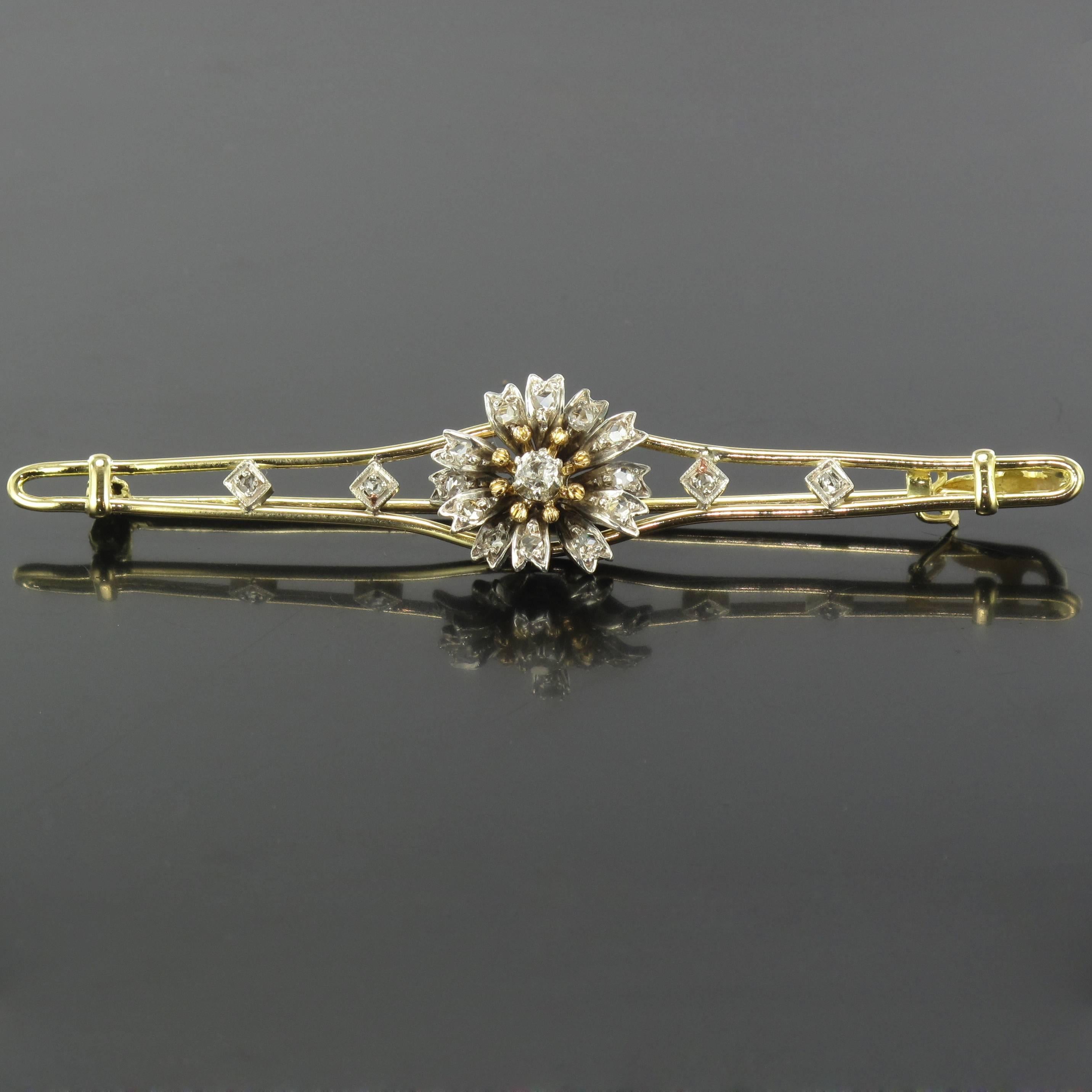 Brooch in 18 carat yellow gold and silver. 
Formed of a flower of which the heart is set with an antique cut diamond with rose cut diamonds in the petals, the flower is set on 2 golden strands held at each side by 2 x 2 rose cut diamonds. At each
