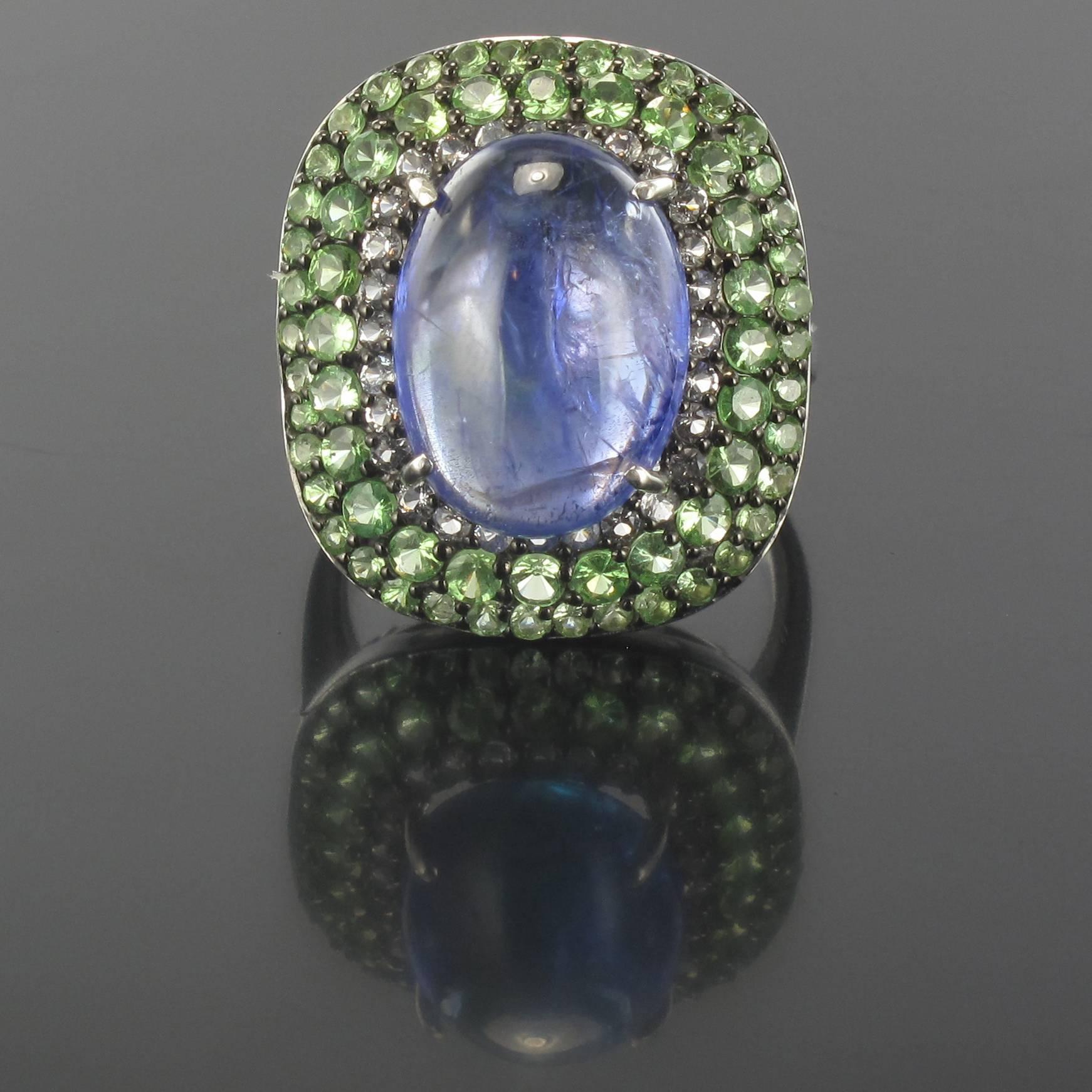 Silver Ring.

This sparkling silver ring is claw set with a Tanzanite cabochon surrounded by a double row of tsavorite green garnets and a row of white topazes. The bed of this tanzanite ring is openwork to allow light to enter beneath the