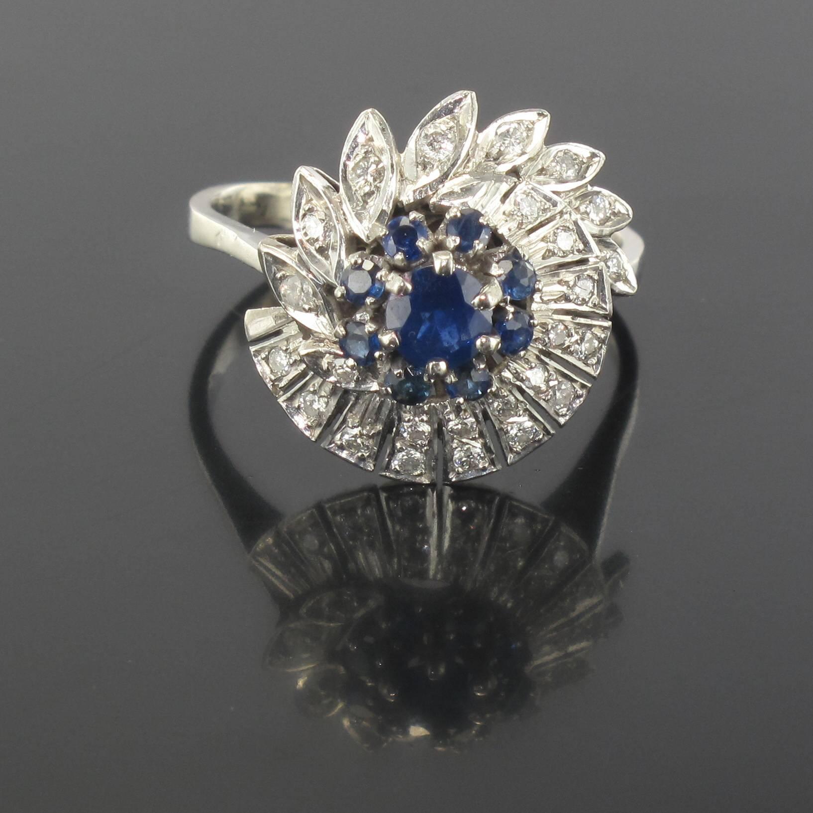 Platinum ring, dog hallmark.

This ring is set with a round sapphire surrounded by 8 small blue sapphires. The head is bordered by a spiral that is set with diamonds in a bar type design on one side and marquise design on the other. 

Total