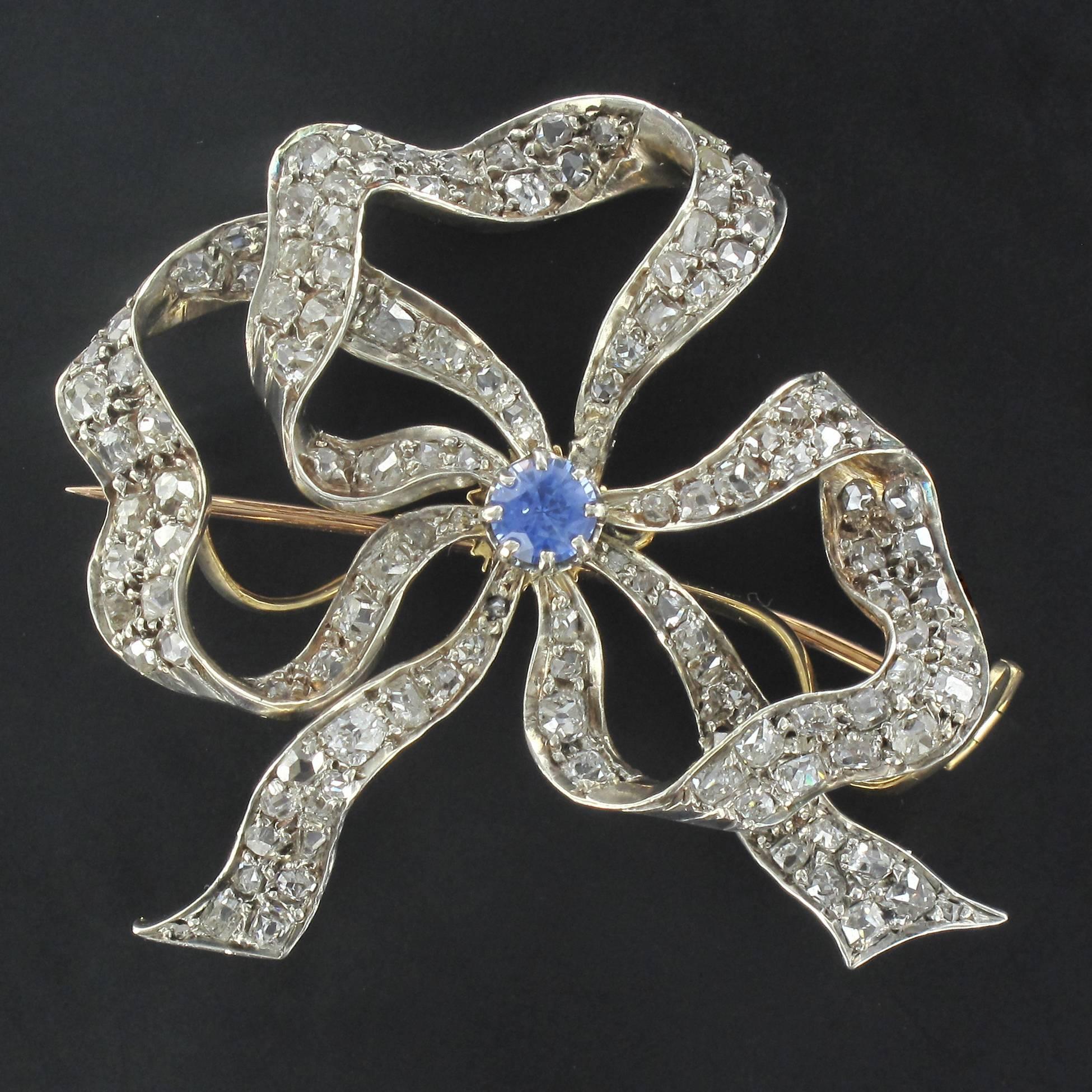 Pair of brooches in 18 carat yellow and pink gold and silver.

Each antique brooch is in the form of an openwork bow that is covered with rose cut diamonds and boasts a claw set round sapphire at the centre. The brooches each feature a pin clasp as