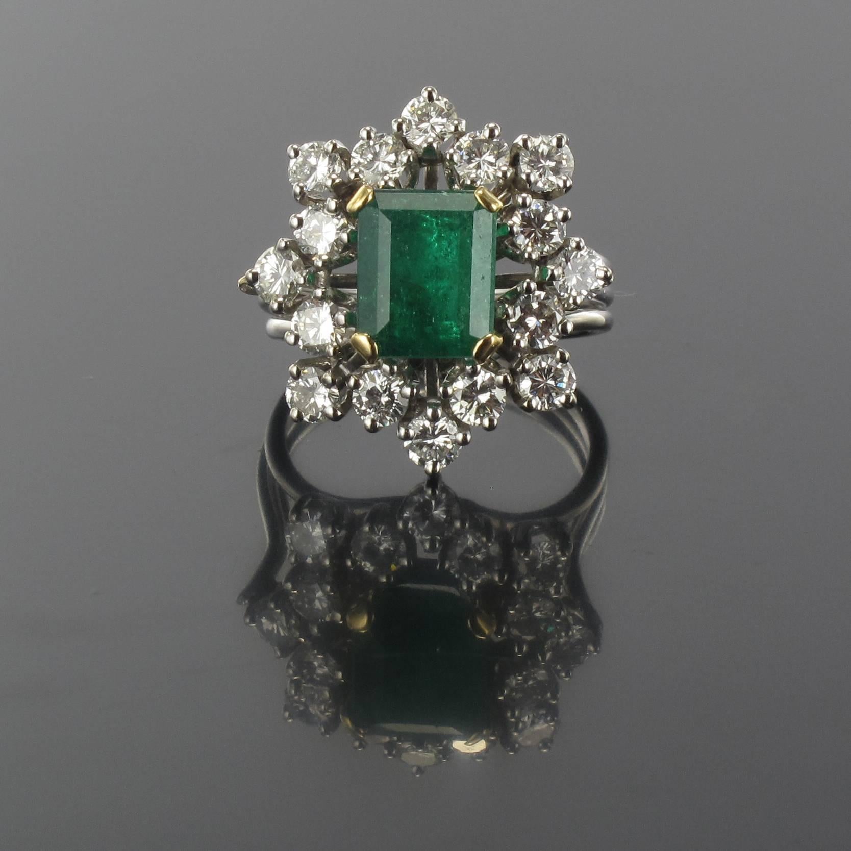 Ring in 18 carat white gold, eagle head hallmark. 

This impressive ring is claw set in yellow gold with an emerald cut emerald surrounded with 16 claw set brilliant cut round diamonds. The ring band is composed of three white gold strands that