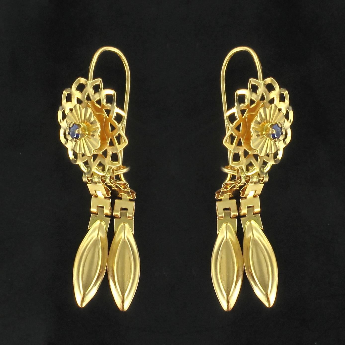 Earrings in 18 carat yellow gold. 

These earrings feature a round flower motif in openwork, chiselled whirls of golden strands from which are asymmetrically suspended 2 chains of flat square openwork links ending each in a faceted golden