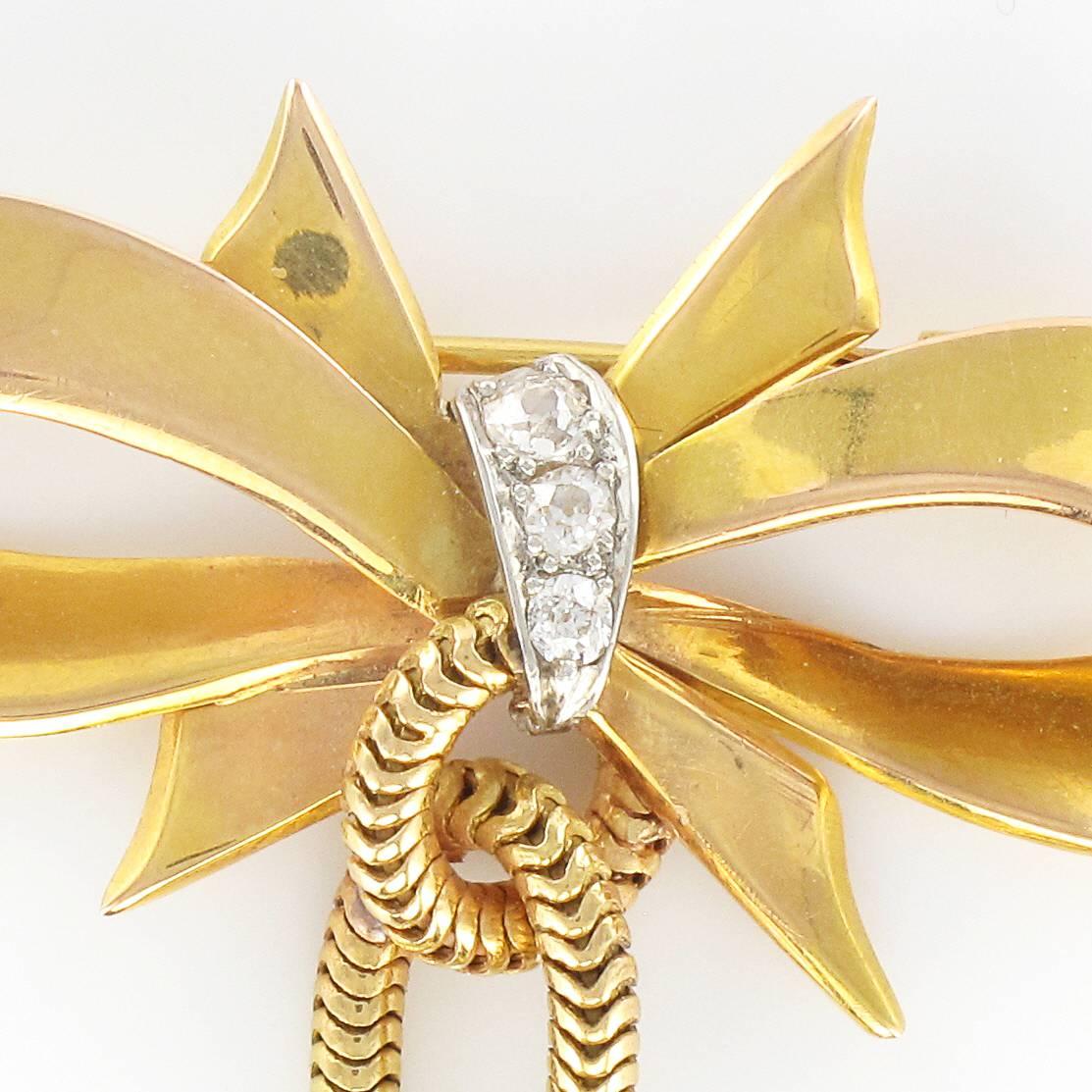 Brooch in 18 carat yellow gold.
This tank brooch in the form of a bow features a central strap set with diamonds. At its base a looped snake chain is finished at each end with a golden bead and cone. It has a pump clasp. 
Width at widest: 3.3 cm,