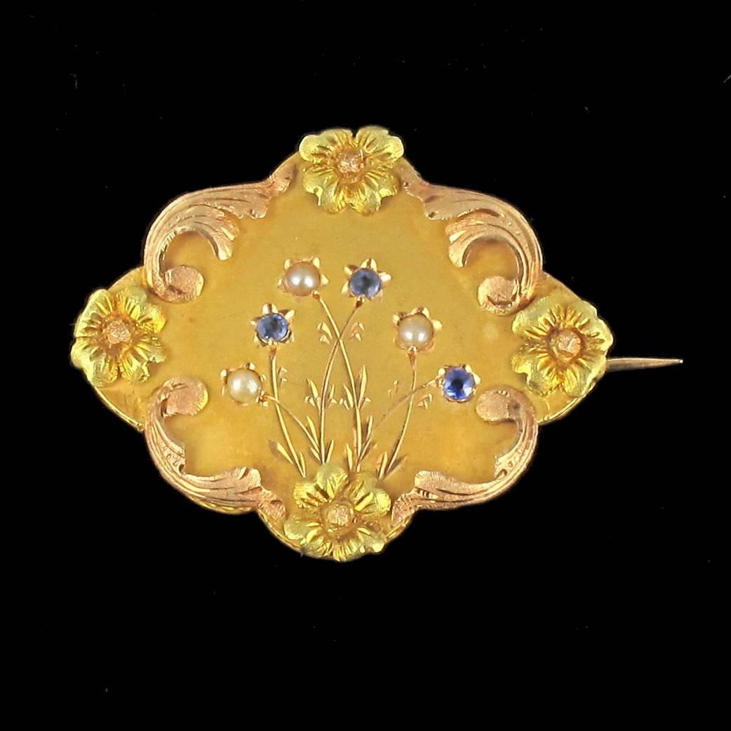 Brooch in 18 carat yellow rose and green golds, eagle head hallmark. 

This fabulous Art Nouveau brooch is composed of an octagonal shaped gold plate set with 3 fine half pearls and 3 round blue sapphires within an engraved plant motif. The edge