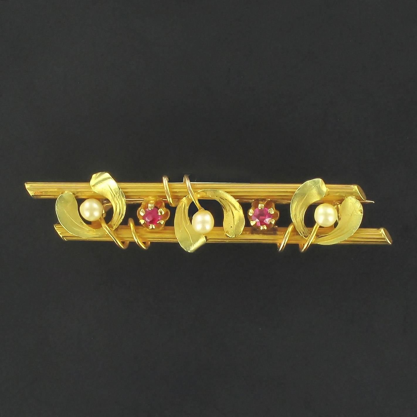 Brooch in 18 carat yellow gold, eagle head hallmark. 

Stupendous barrette brooch that is composed of 2 gold cylinders with a chiselled motif entwined by 3 matt gold leaves set with 3 small fine pearls and interspersed with 2 claw set red gems. It