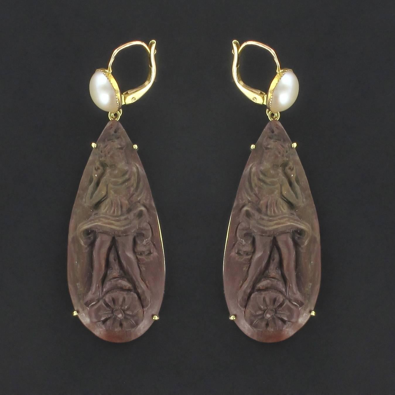 Earrings in yellow gold, 750 thousandths, 18K.

These splendid dangle earrings are each composed of a beaded sleeper setting with a half white oriental cultured pearl from which is suspended a tear shaped brown cameo in lava stone. Each cameo