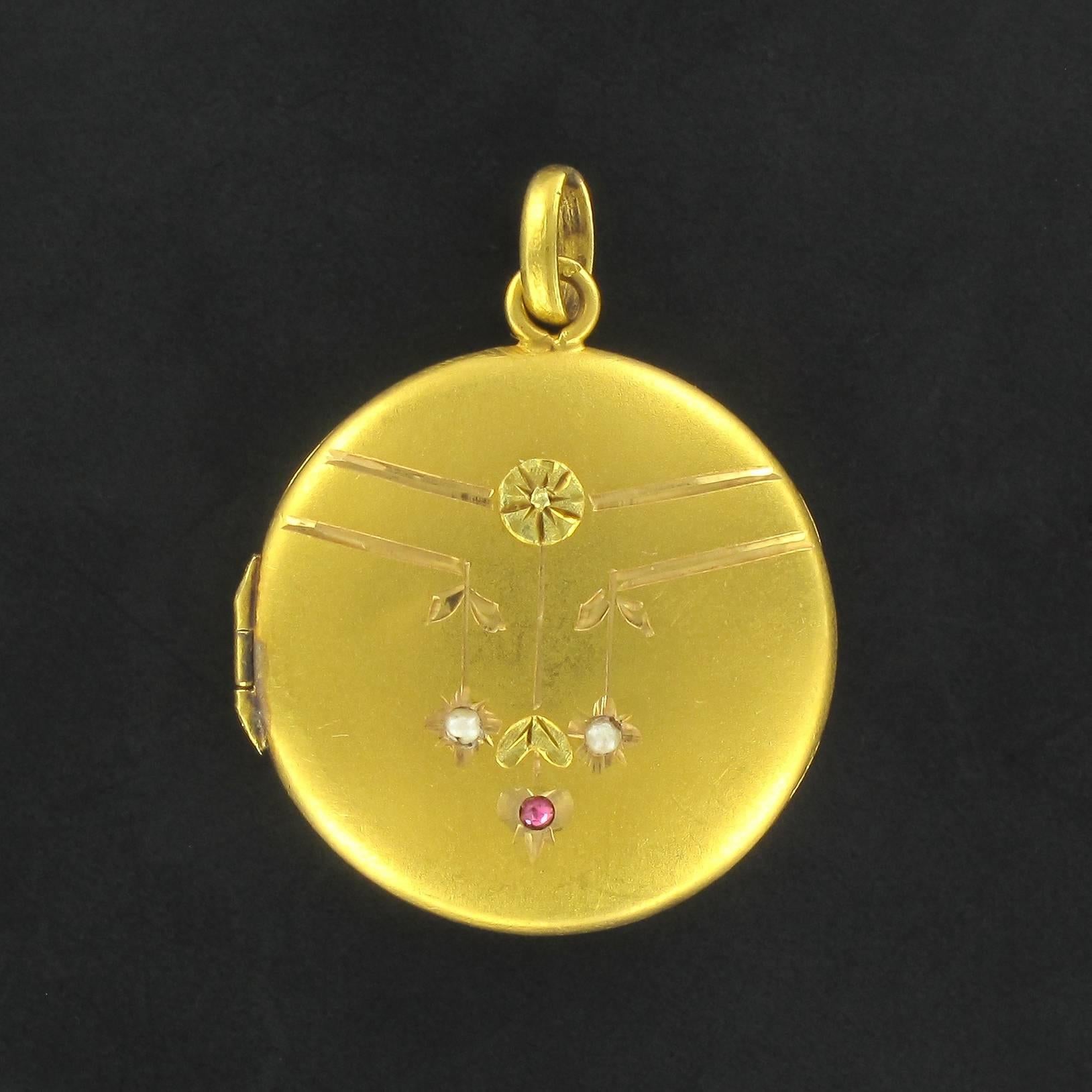 Medallion in 18 carat yellow gold. 
A charming item of antique jewellery, this gold pendant is round and engraved at the front with a floral motif set with 2 fine half pearls and a small ruby. It opens at the side with a hinge. You are thereby able