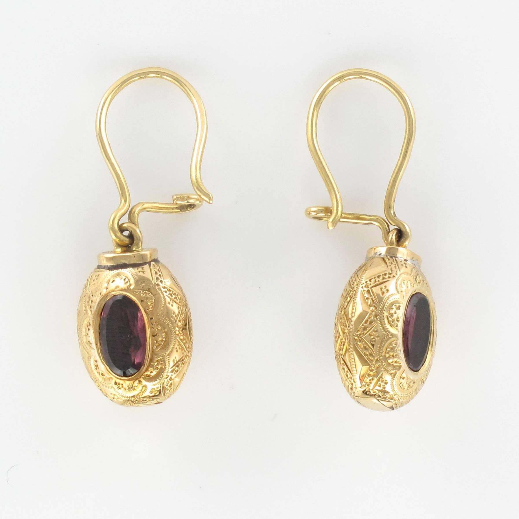 Earrings in 18 carat yellow gold. 

Each of these antique earrings is formed of a finely engraved oval design set with a central garnet. The clasps are goosenecks with safety hooks. 

Height: 2.9 cm, width at widest: 0.97 cm.
Weight: about 4.1