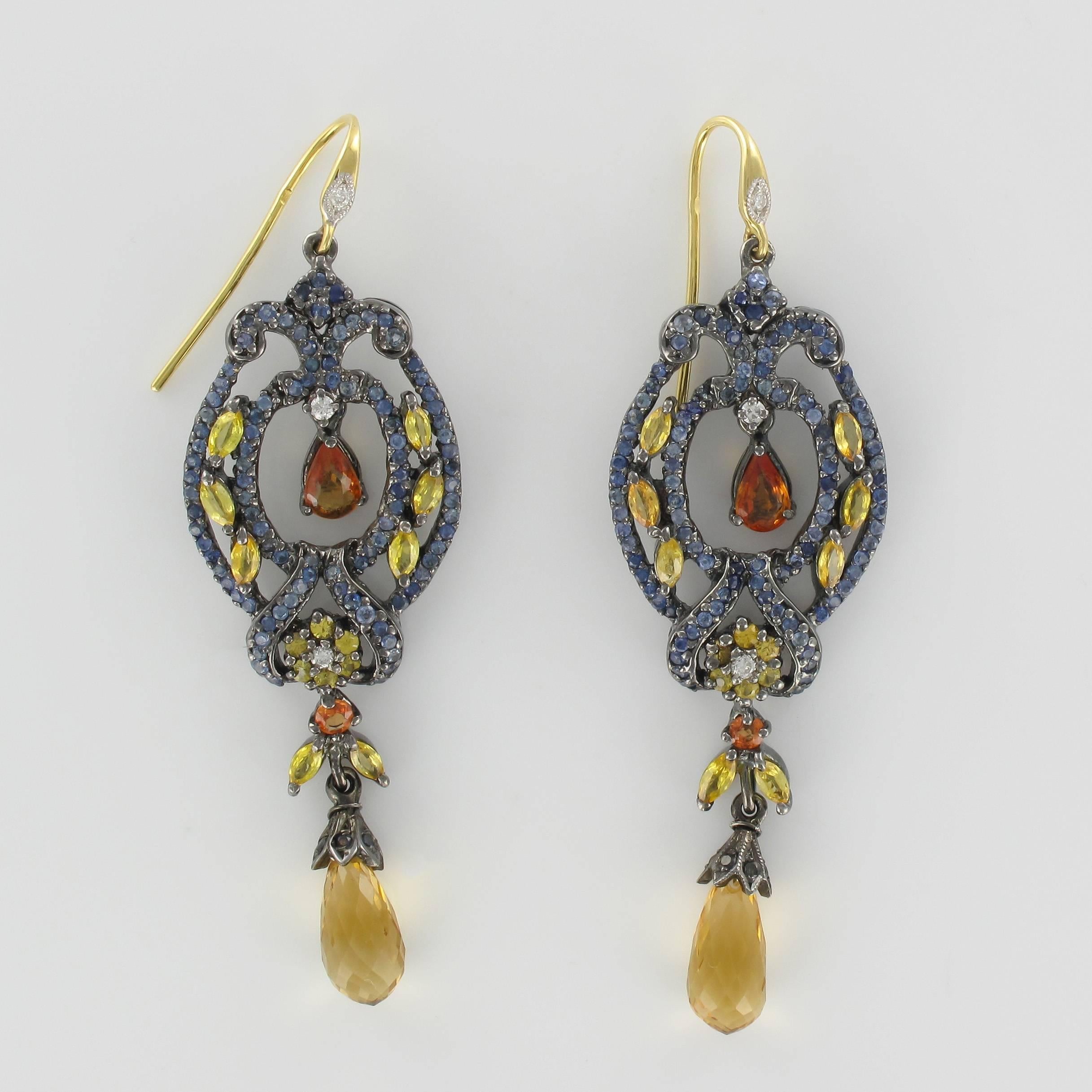 Pair of earrings in silver and yellow gold.

Each dangle earring is set with 221 blue sapphires, 2 orange sapphires, 46 yellow sapphires and 4 brilliant cut diamonds in an arabesque design. These earrings feature goose neck fittings each set with a