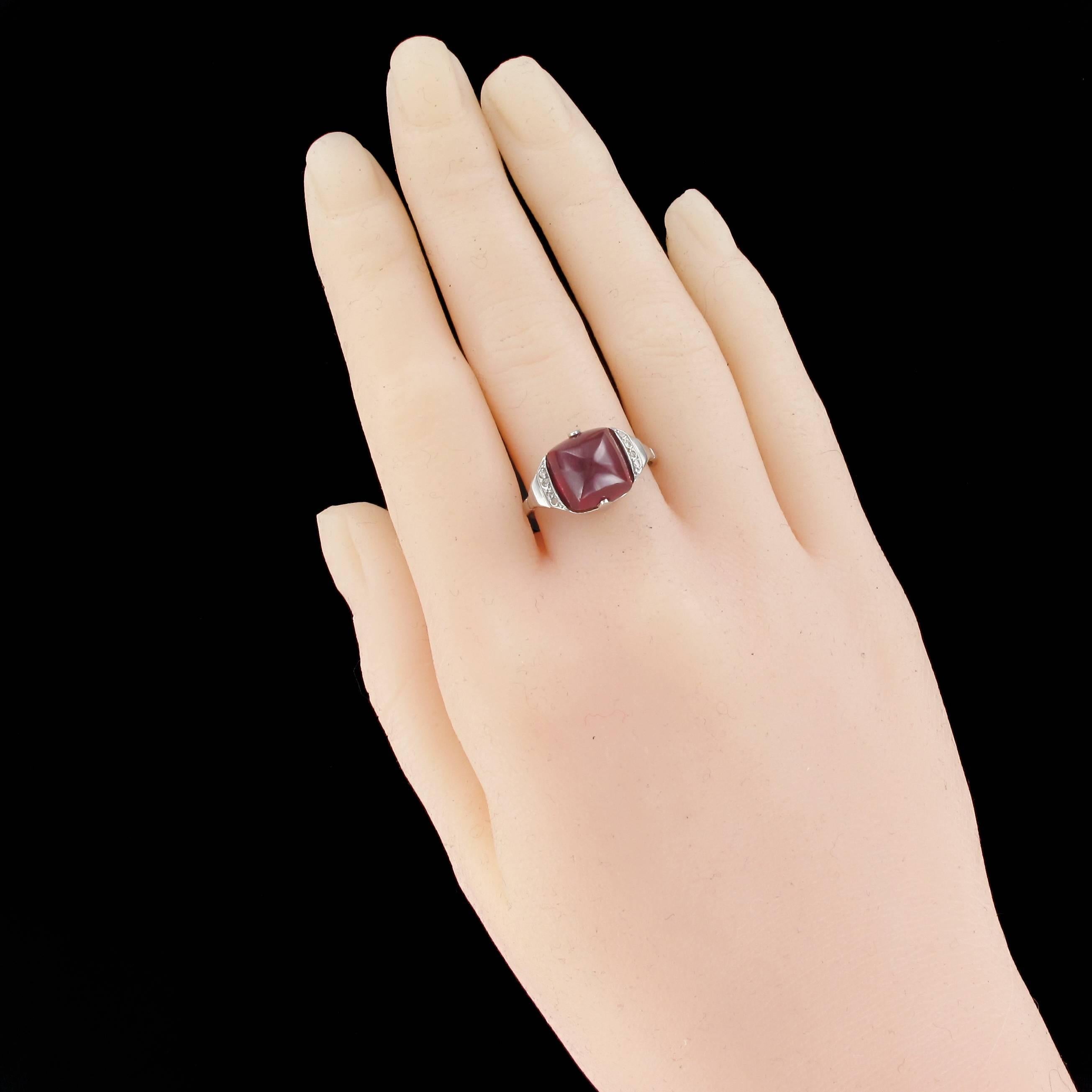 Ring in 18 carat white gold, eagle head hallmark.

This splendid antique ring is set with a sugar loaf shaped ruby cabochon. At each side is a line of 4 rose cut diamonds. The beginning of the ring band on each side has a chiselled geometric design.